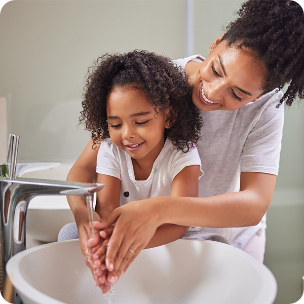 woman helping a young girl wash hands in a bathroom sink