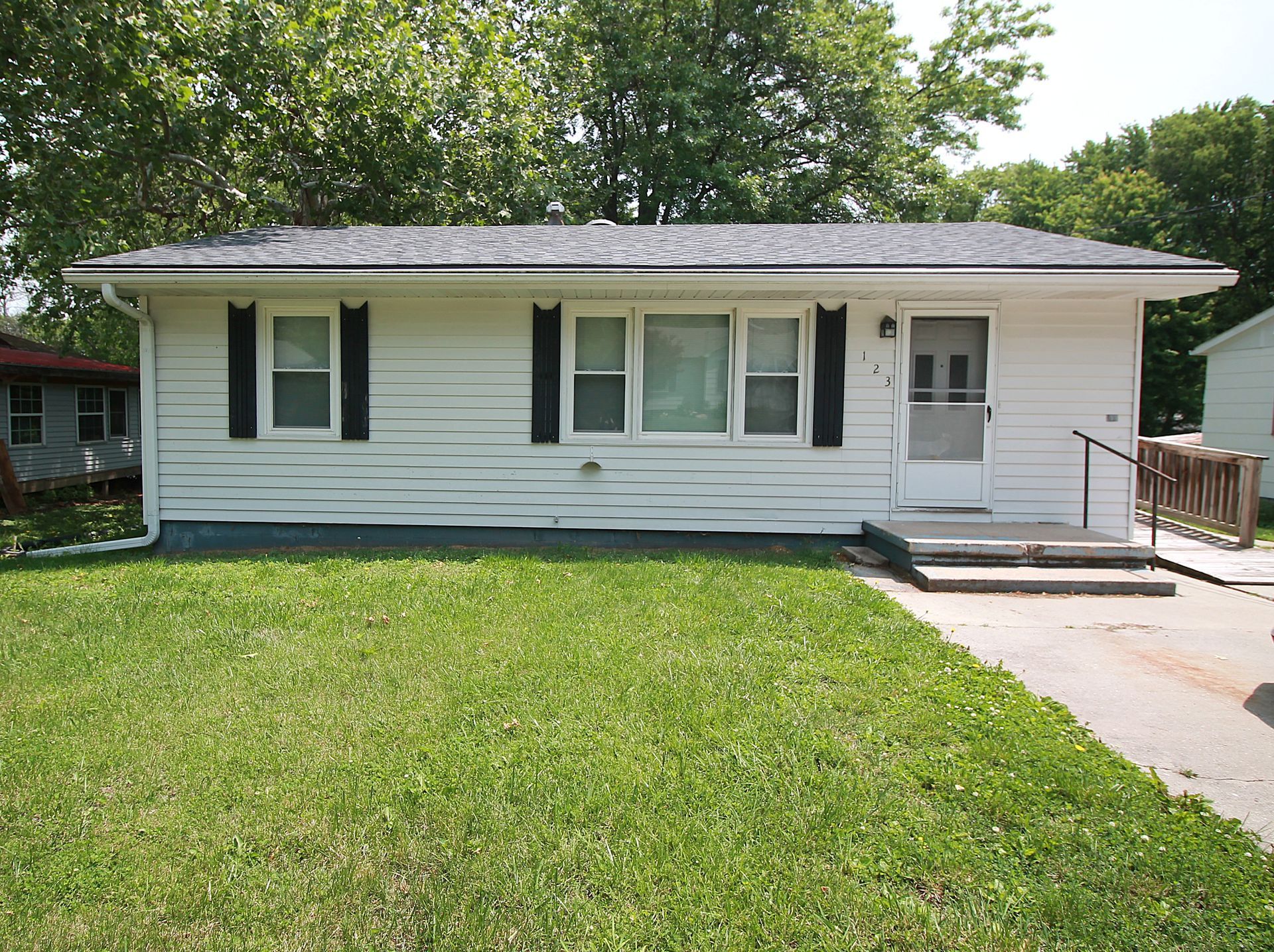 A small white house with black shutters is sitting on top of a lush green lawn.