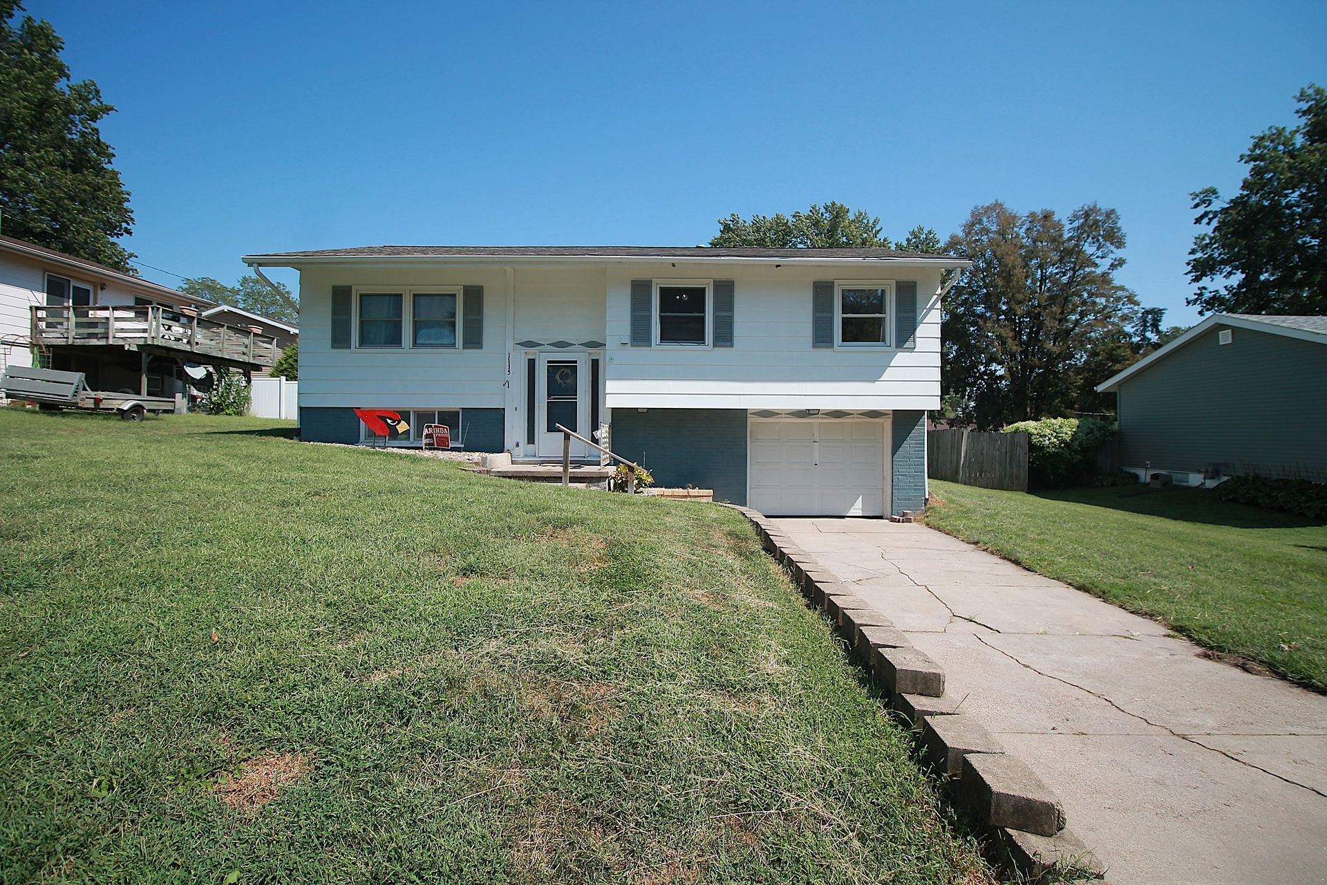 Suburban split-level house with white siding, front lawn, and a driveway leading to the garage.
