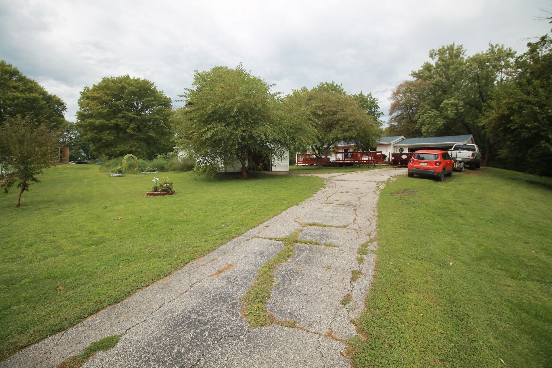 Gravel path through a grassy park to parked cars and red umbrellas near trees