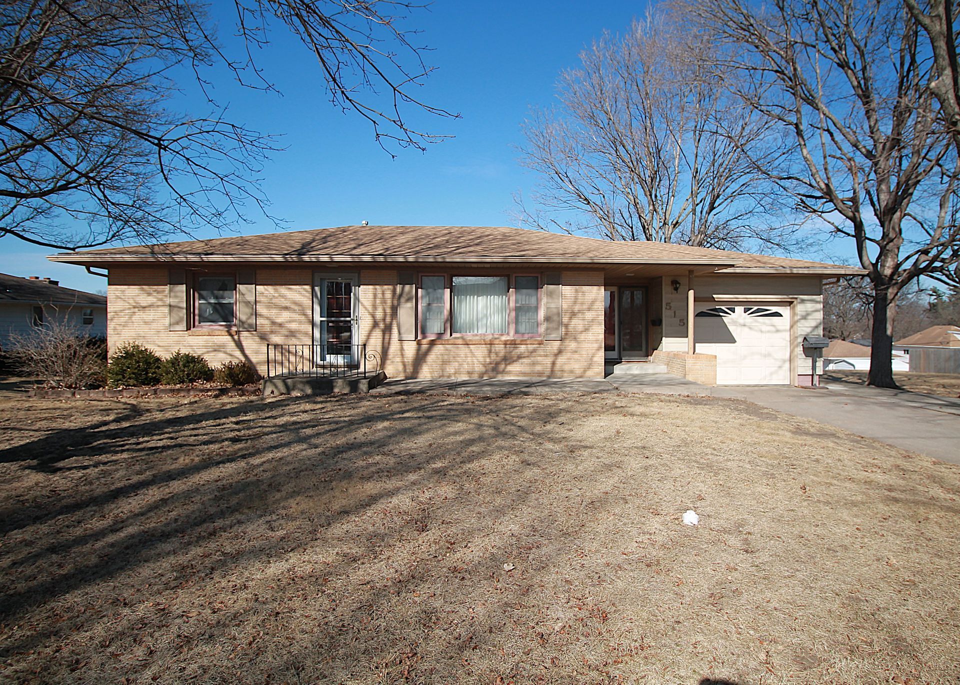 Single-story brick house with a brown roof and a small driveway on a sunny day.