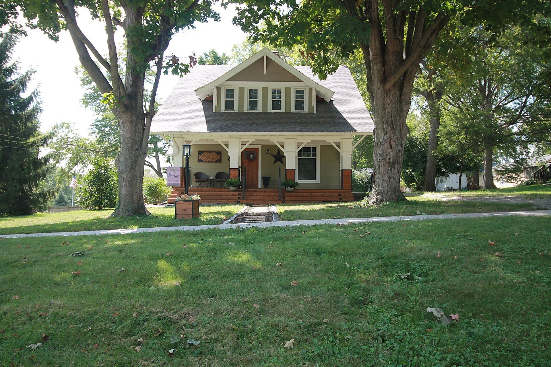 Small white house with a porch and red roof trim, surrounded by a large grassy yard and trees
