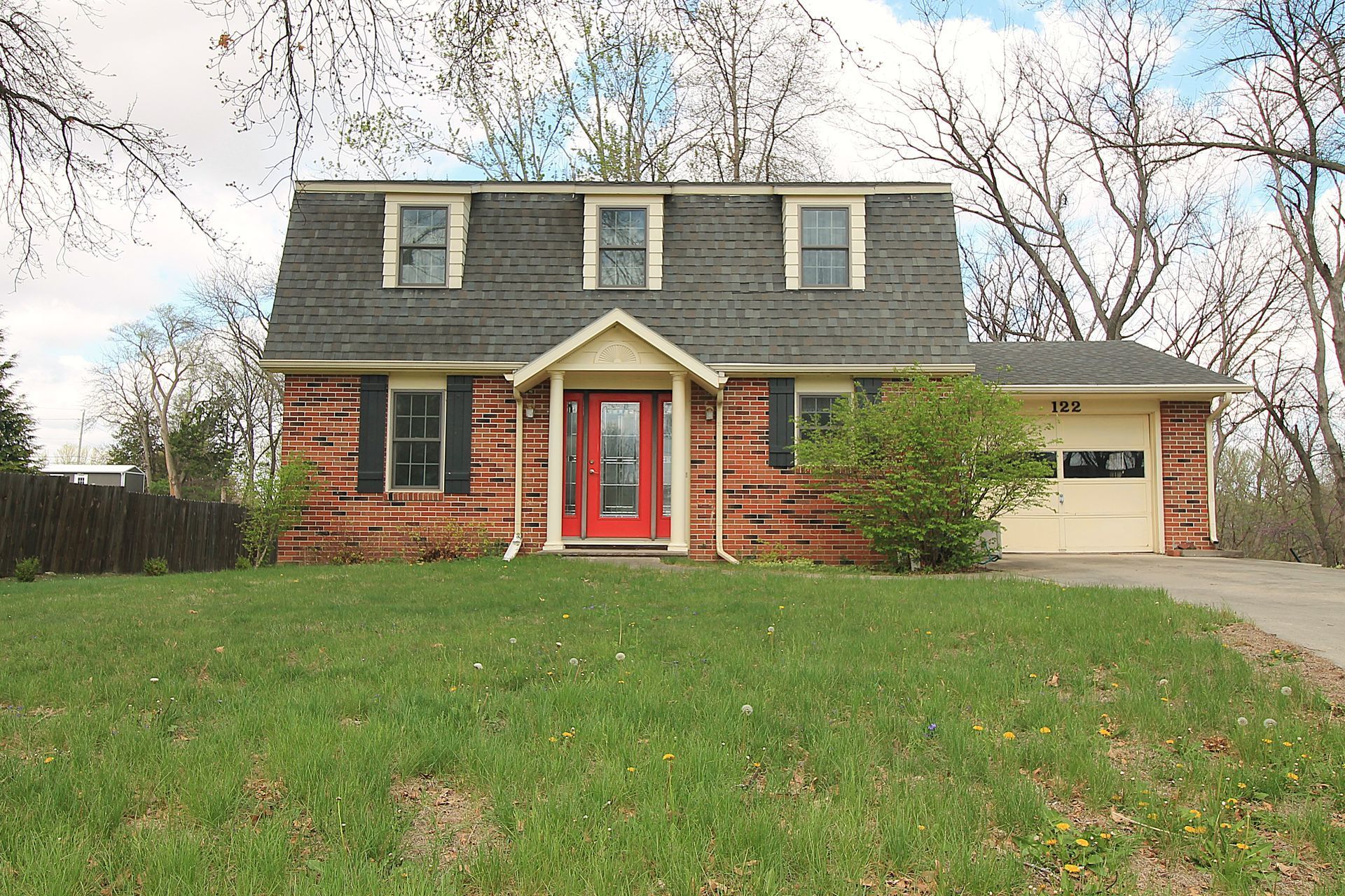 Two-story brick house with red front door, dormer windows, and attached garage on a grassy lawn