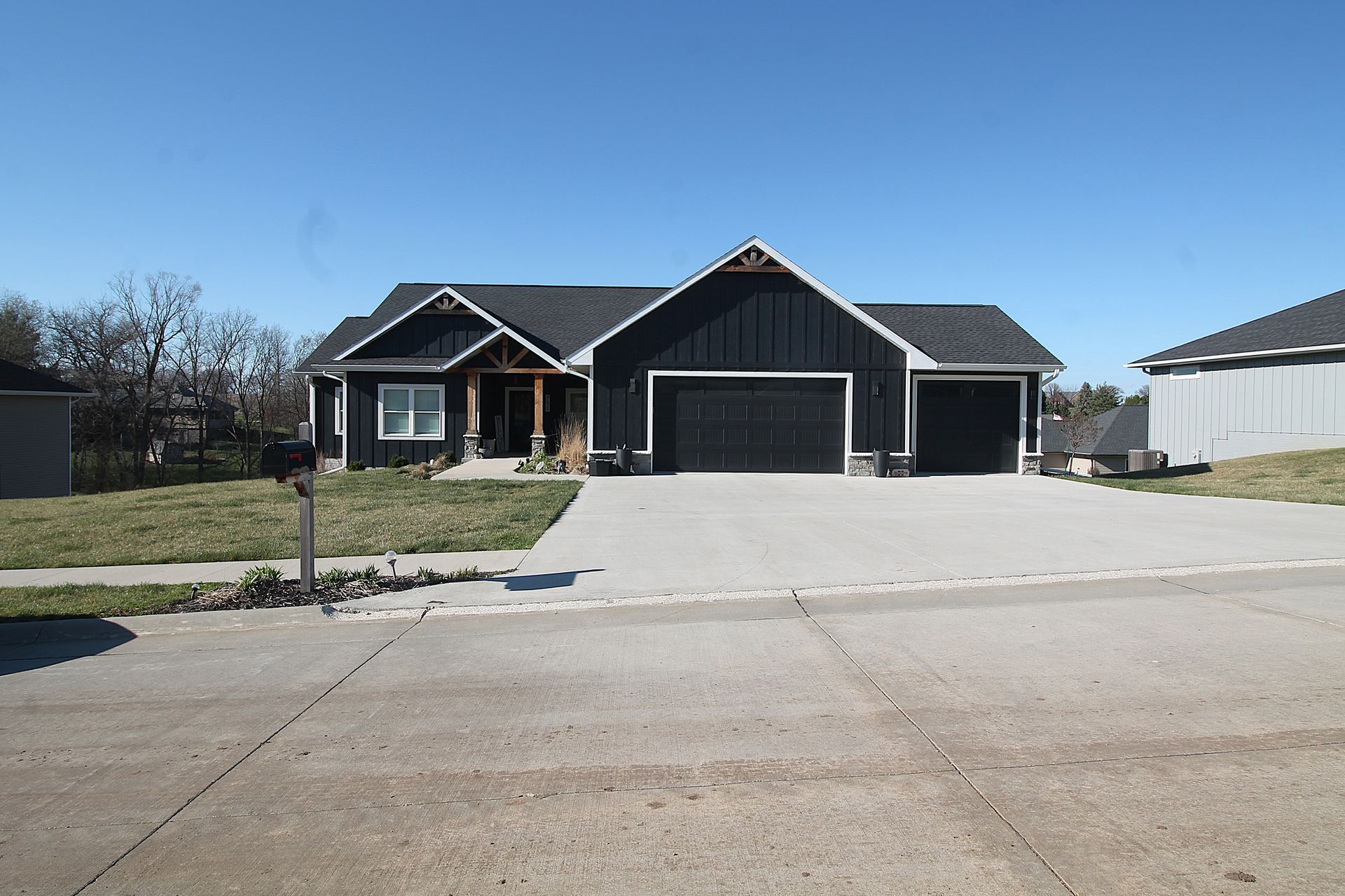 Suburban single-story house with dark roof, double garage, and wide driveway under clear blue sky