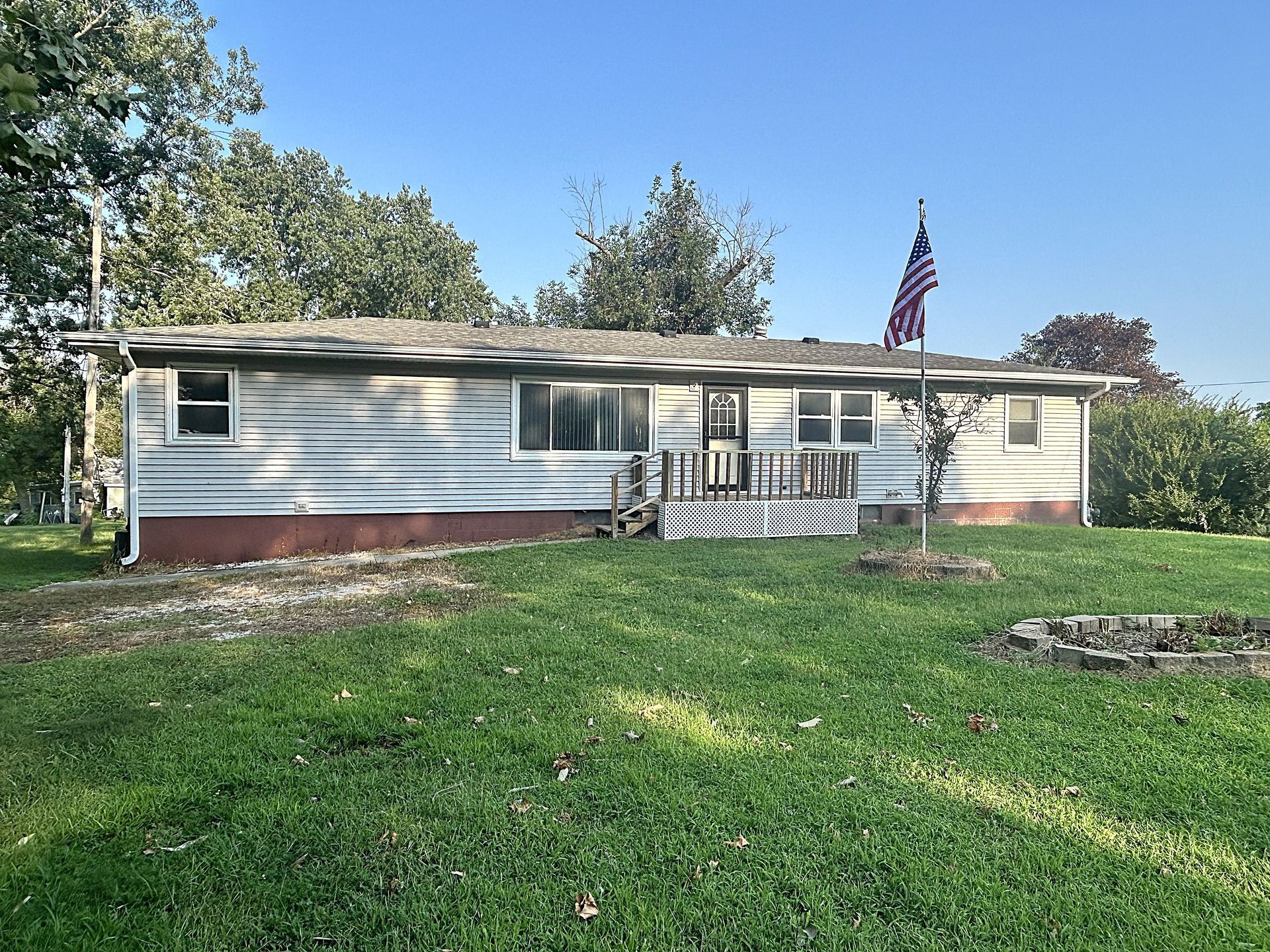 Single-story white house with red brick base, front porch, and American flag, surrounded by a grassy yard.