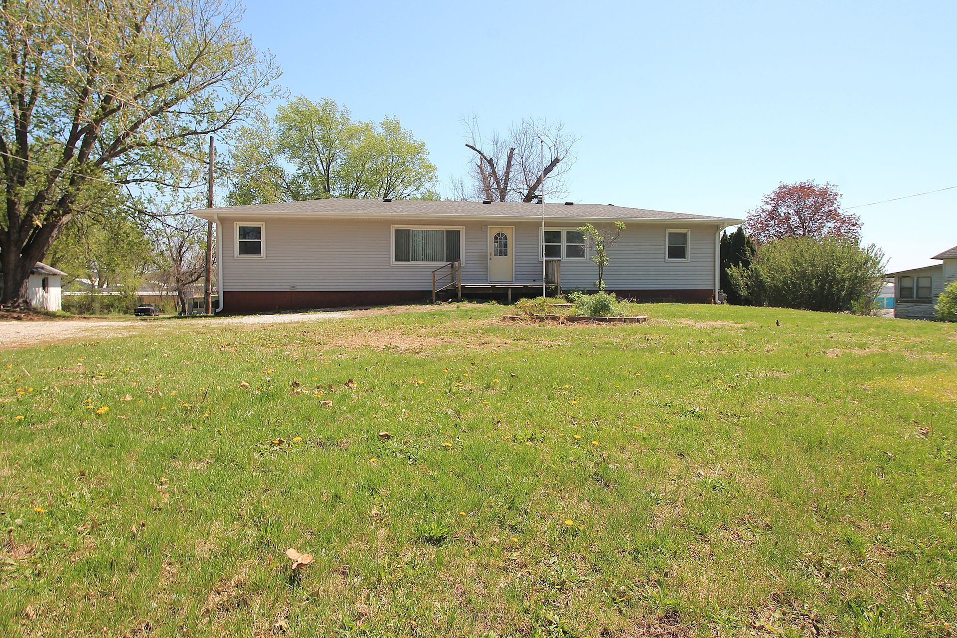 Single-story beige house on a grassy hill with trees in the background