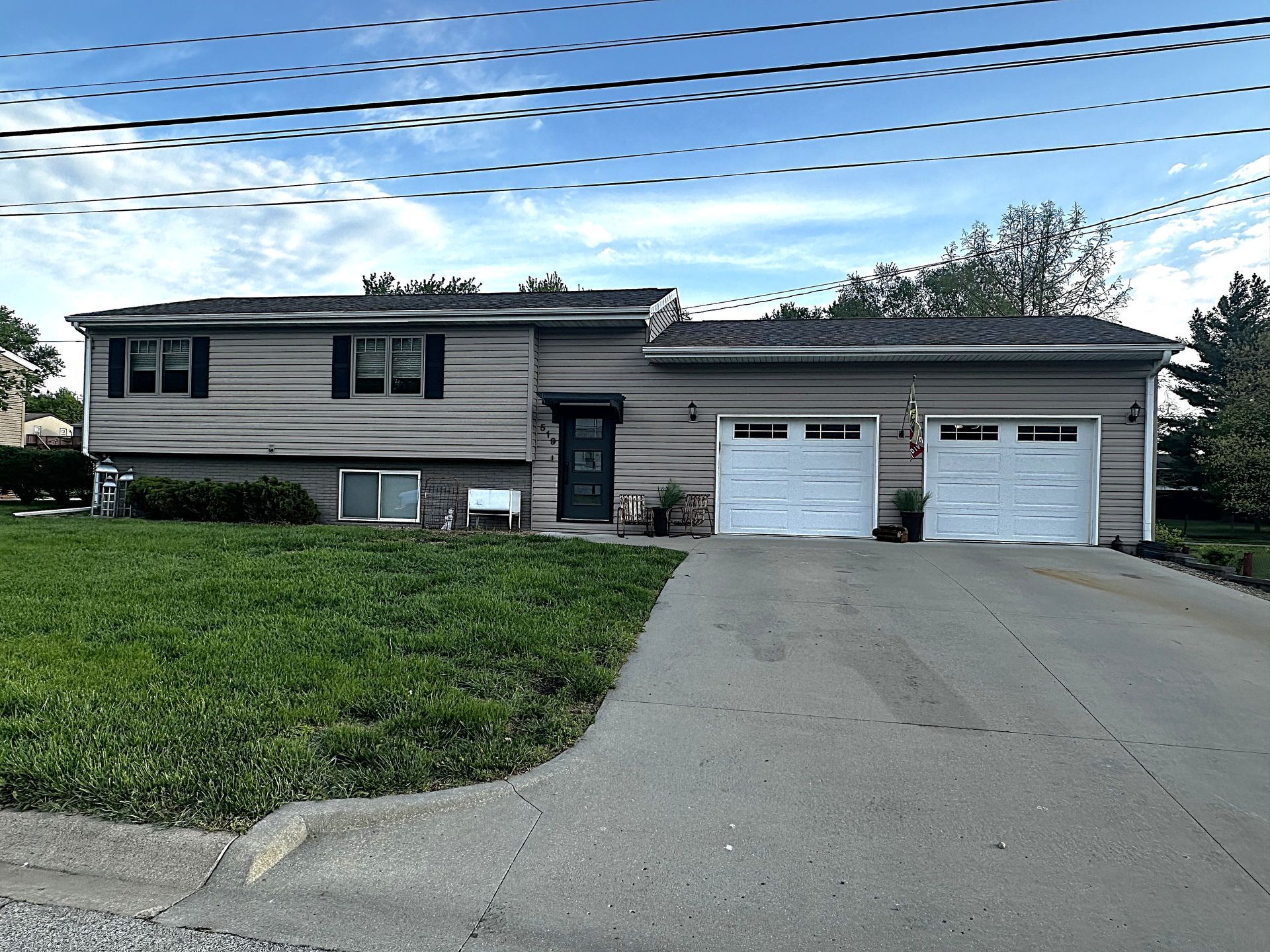 Suburban house with two white garage doors, driveway, and front lawn under a blue sky
