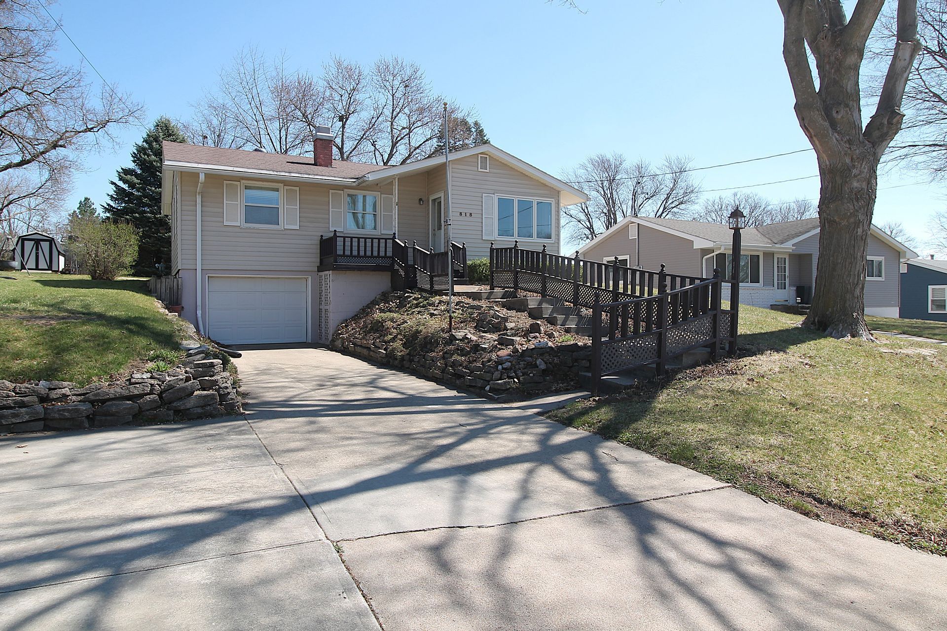 Single-story house with a garage, front steps, and a black fence by a driveway on a sunny day