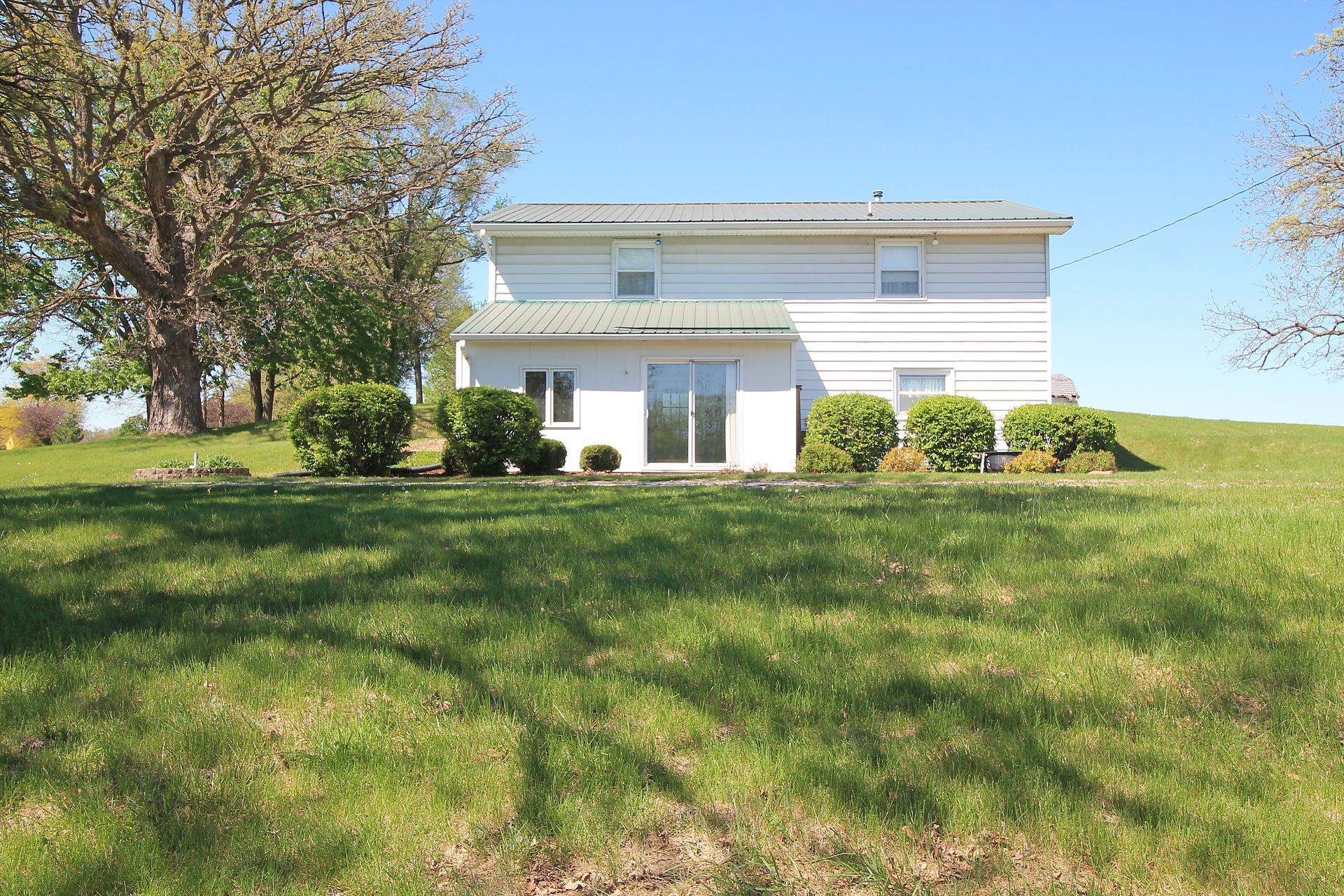 White two-story house with a large green lawn and trees on a sunny day