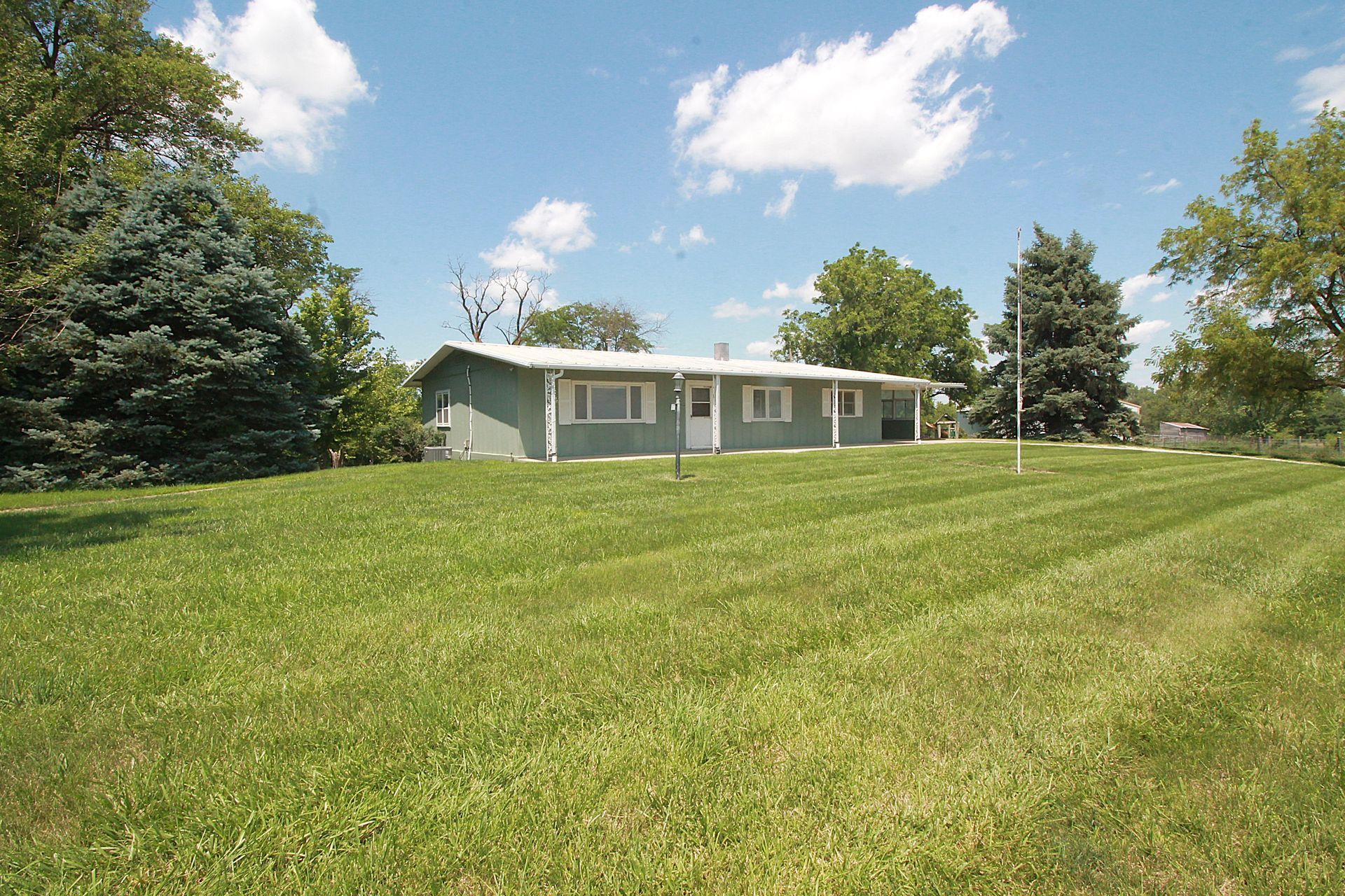 Single-story white house with a large green lawn under a blue sky with clouds