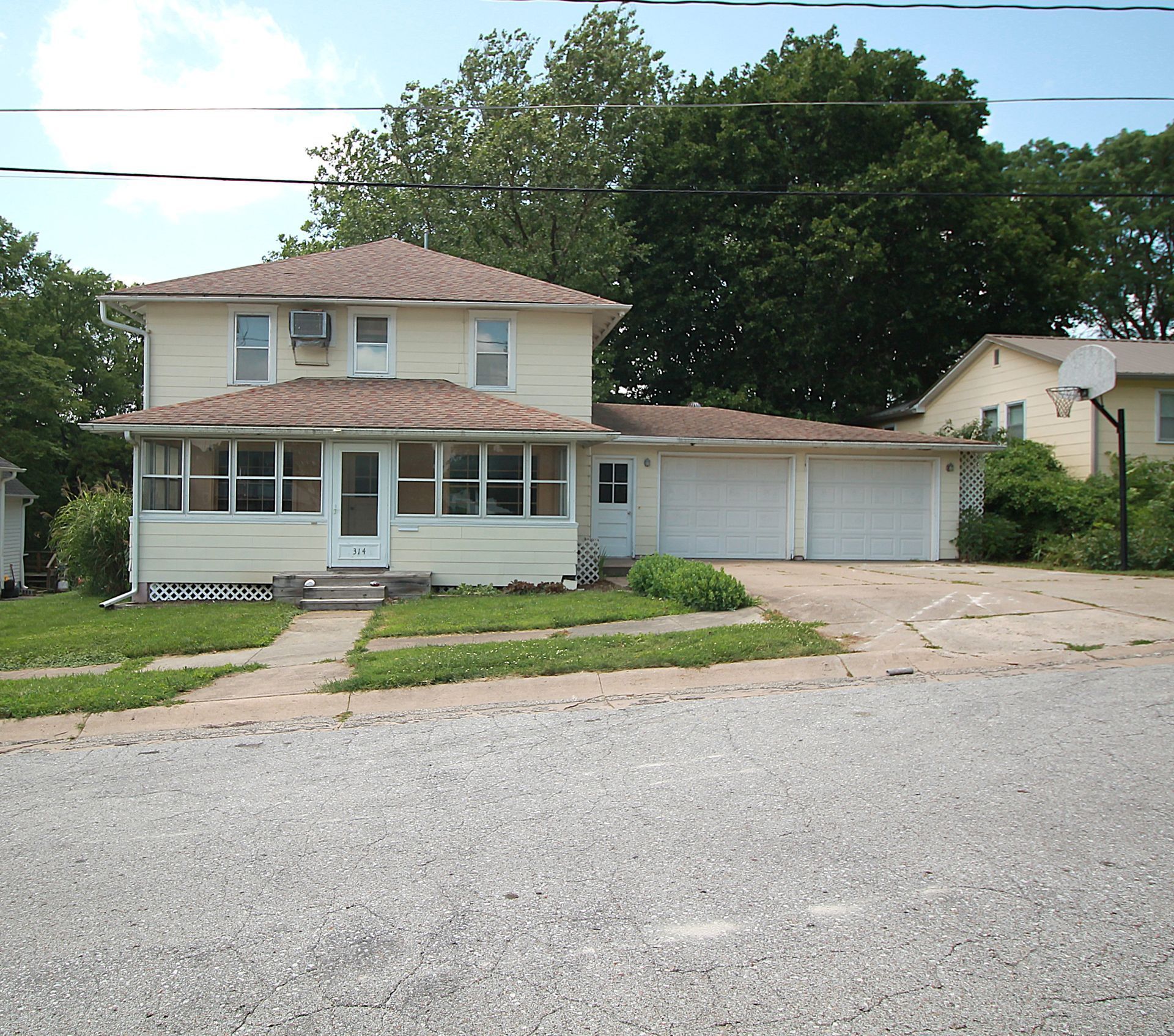 Two-story house with a front porch, attached garage, and driveway on a quiet residential street.
