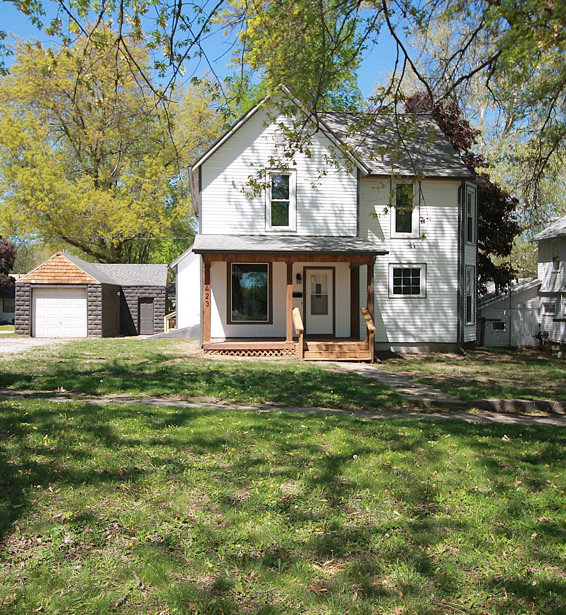 A white house with a porch and a garage is surrounded by trees and grass.