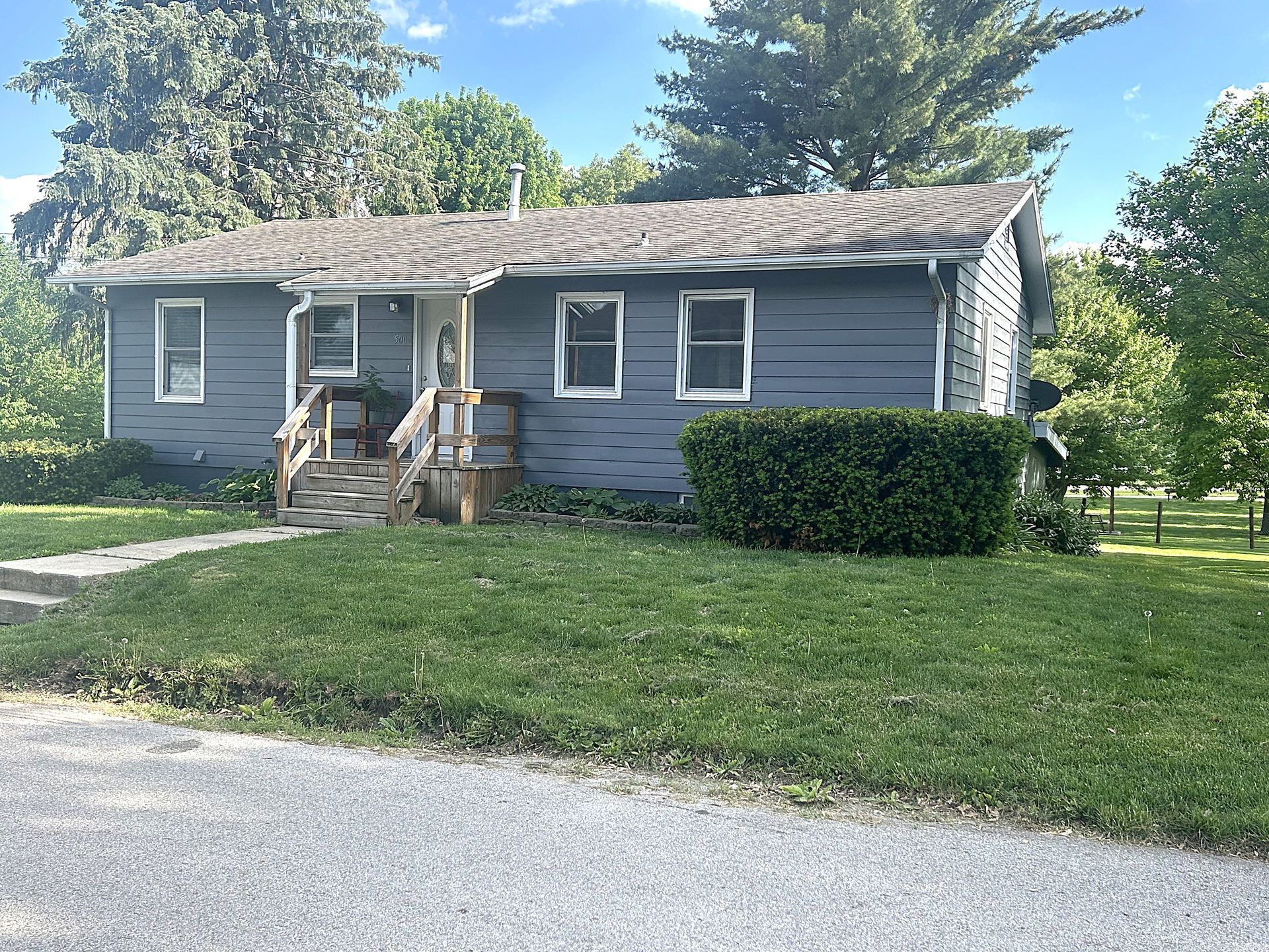 A small gray house with a porch and stairs is sitting on top of a lush green field.