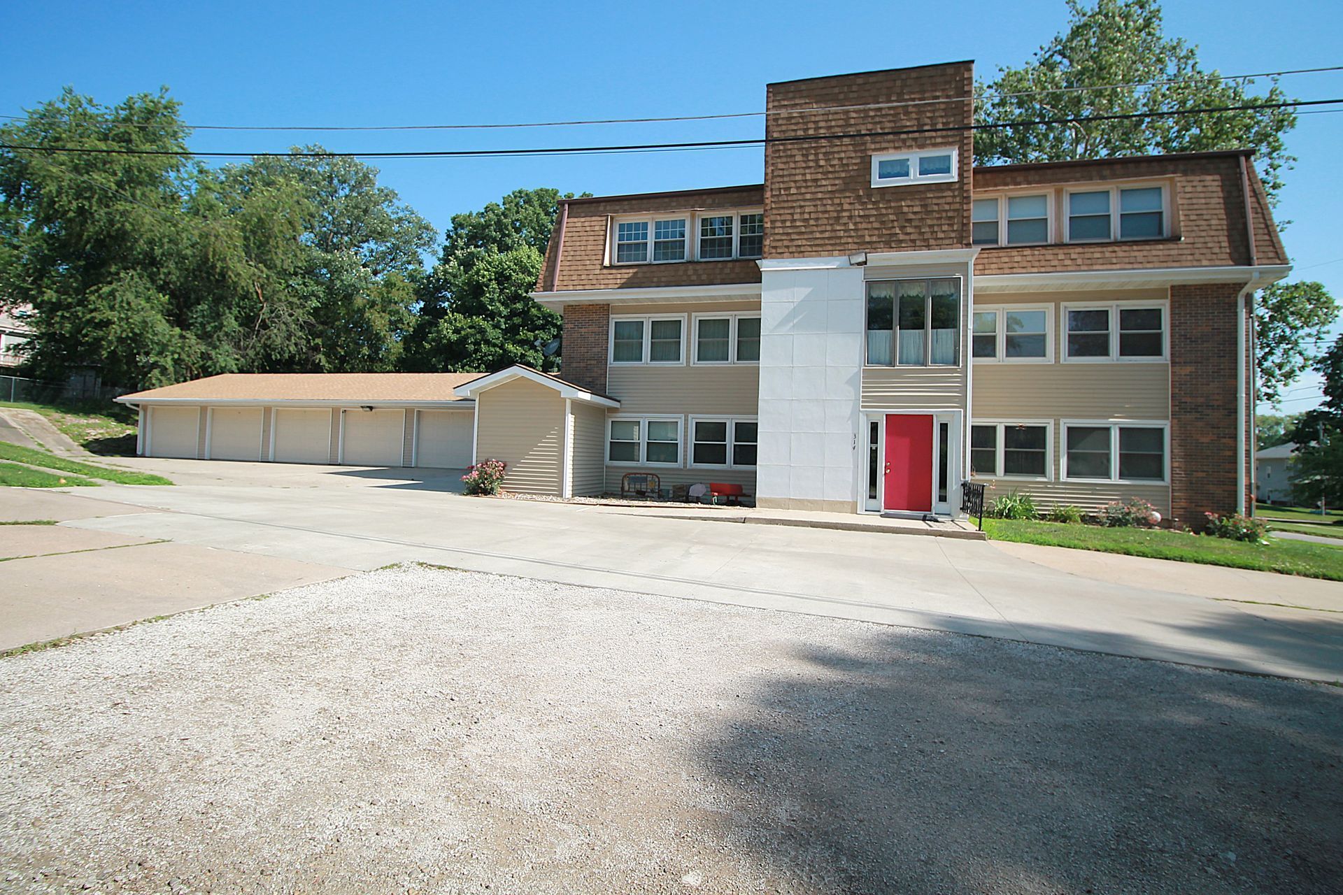 A large house with a red door is surrounded by gravel and trees