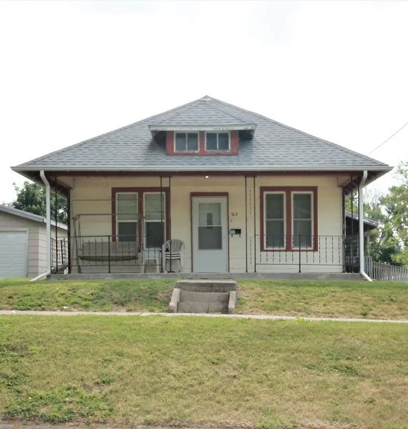 A small house with a gray roof and a bench on the porch