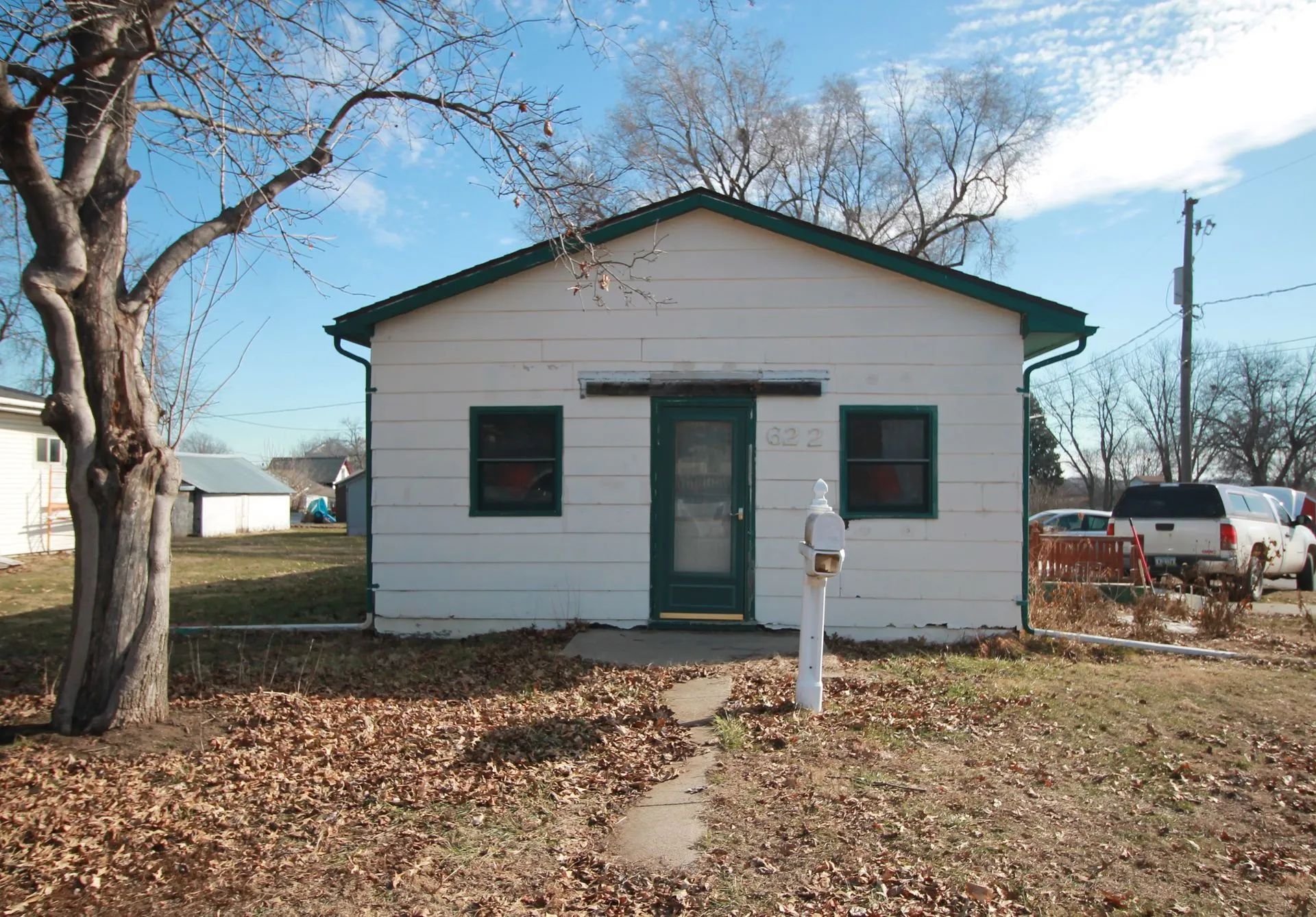 A small white house with a green roof and a tree in front of it