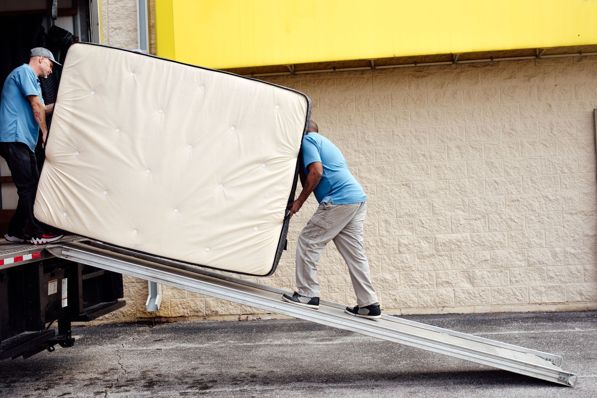 Workers loading a mattress up a ramp into a truck