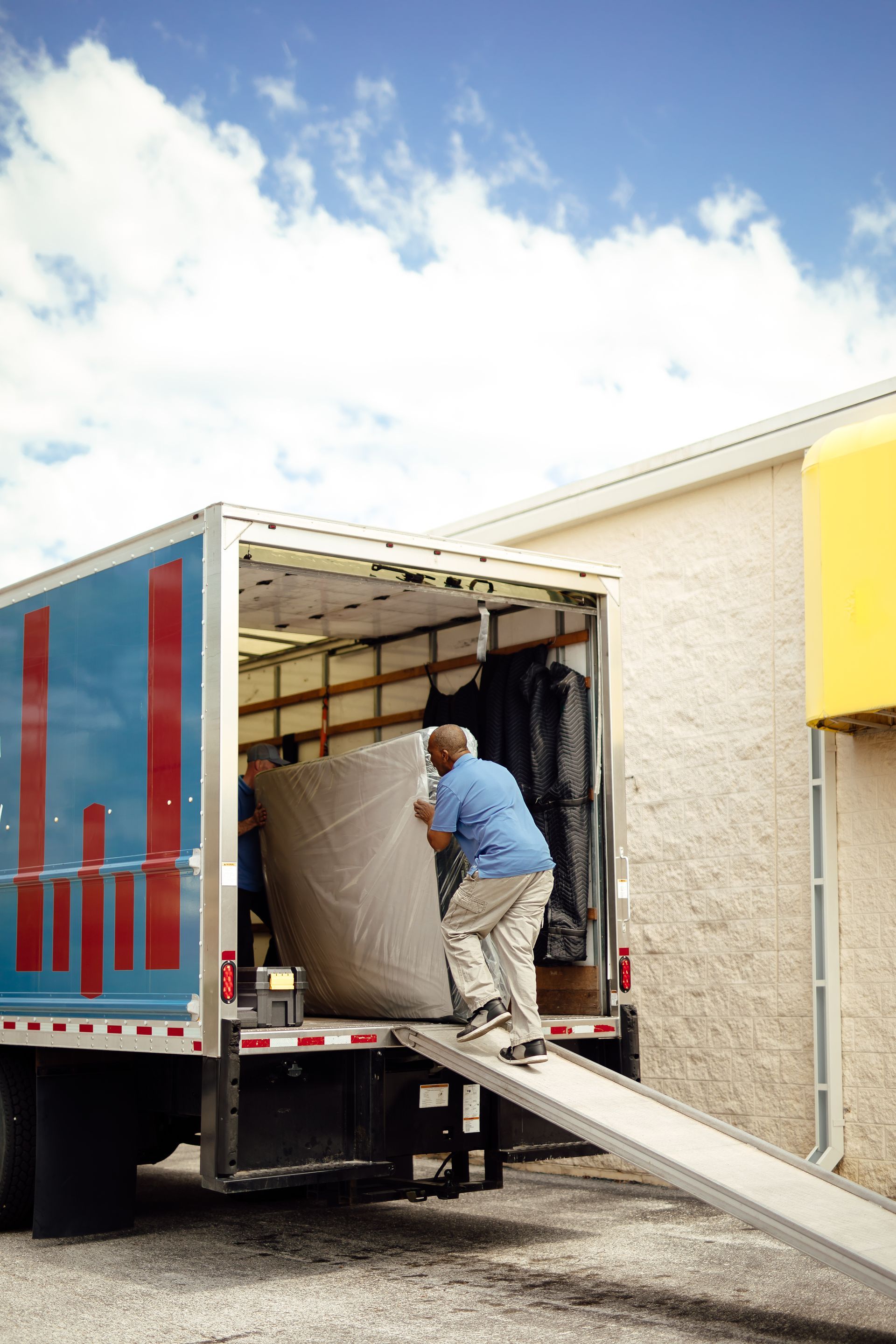 Worker unloading a large object from a moving truck using a ramp outside a building