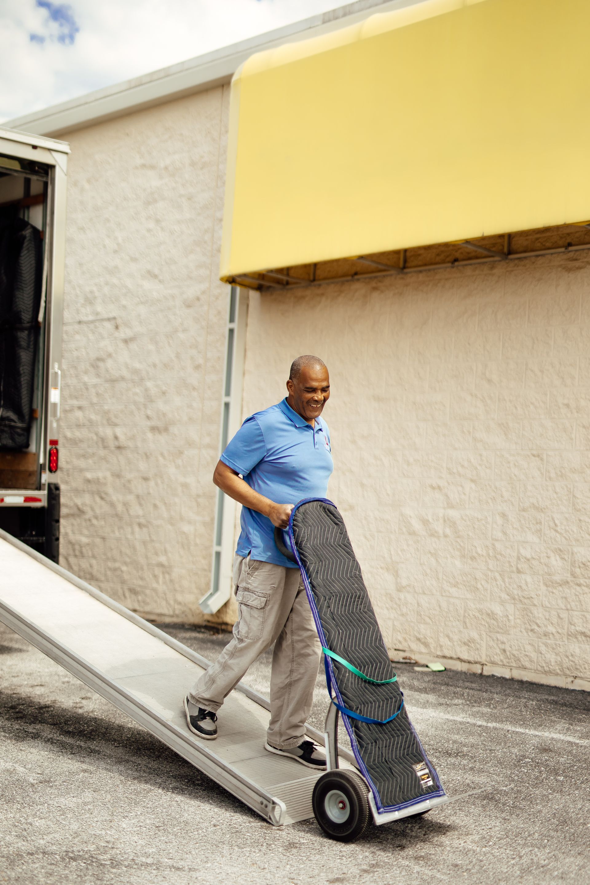 Man pushing a hand truck down a loading ramp beside a building