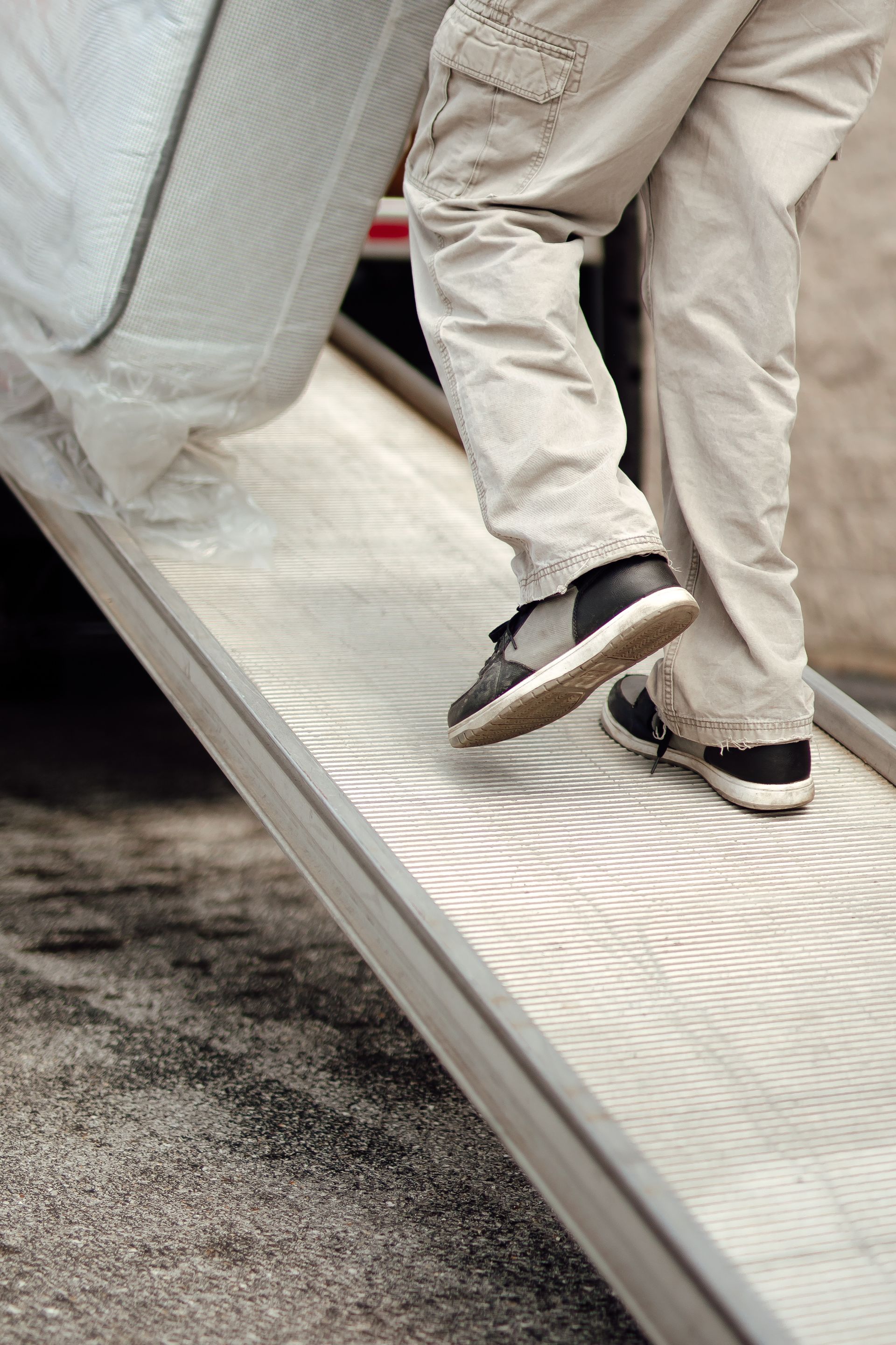People stepping up a metal ramp, close-up of beige pants and black sneakers.
