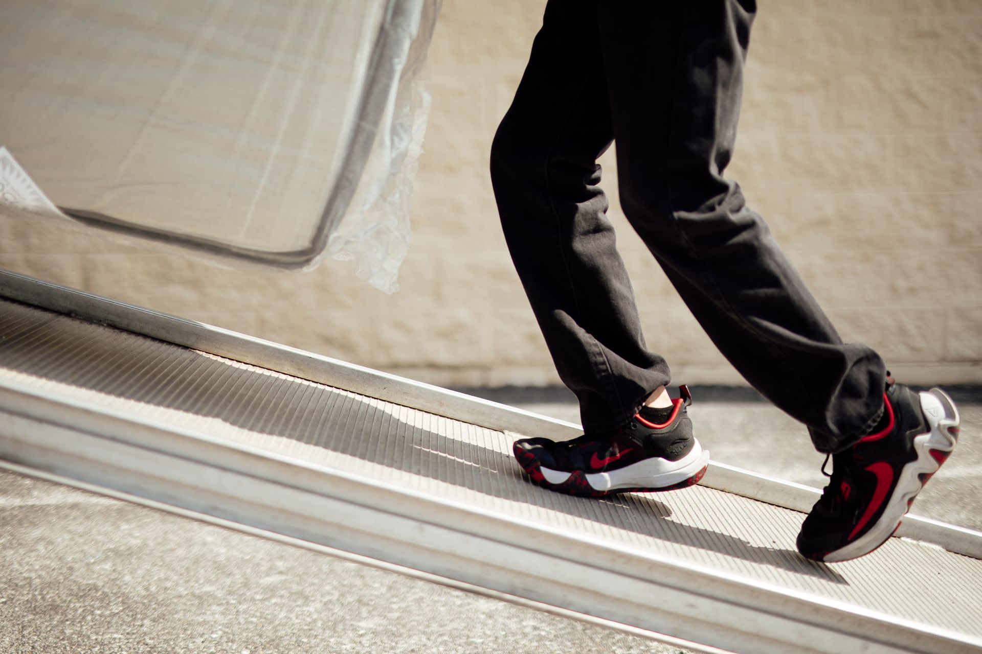 Person walking on a sloped concrete surface in black pants and black-red sneakers