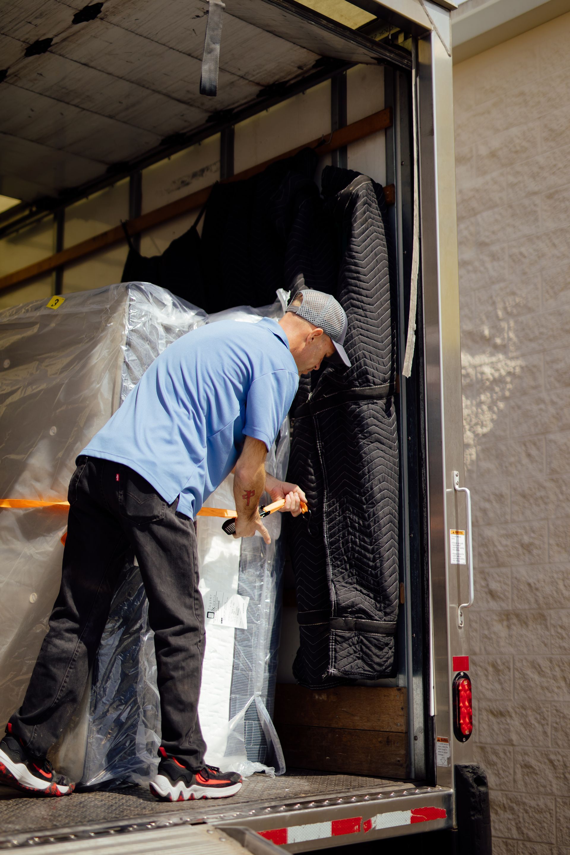 Worker securing a wrapped appliance inside a moving truck with clear plastic and straps.