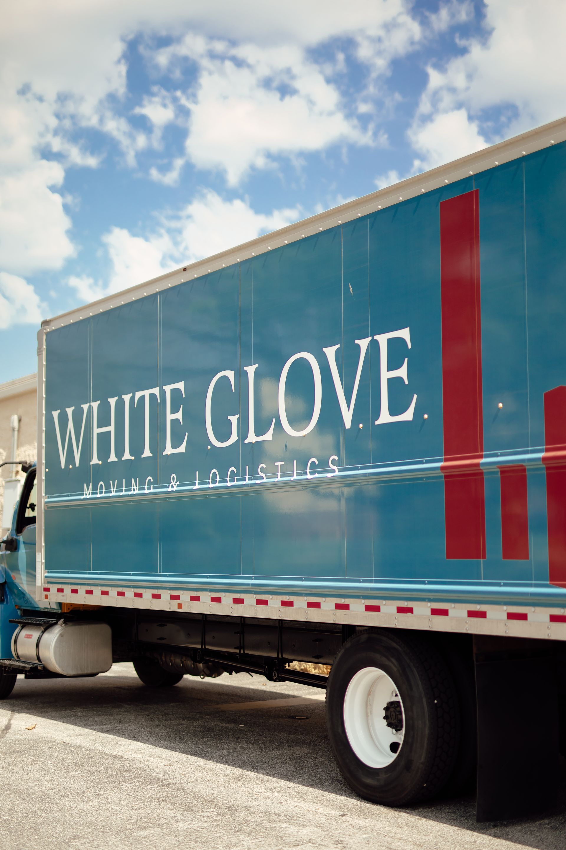 White Glove moving truck with teal trailer and red stripes parked under a partly cloudy sky.