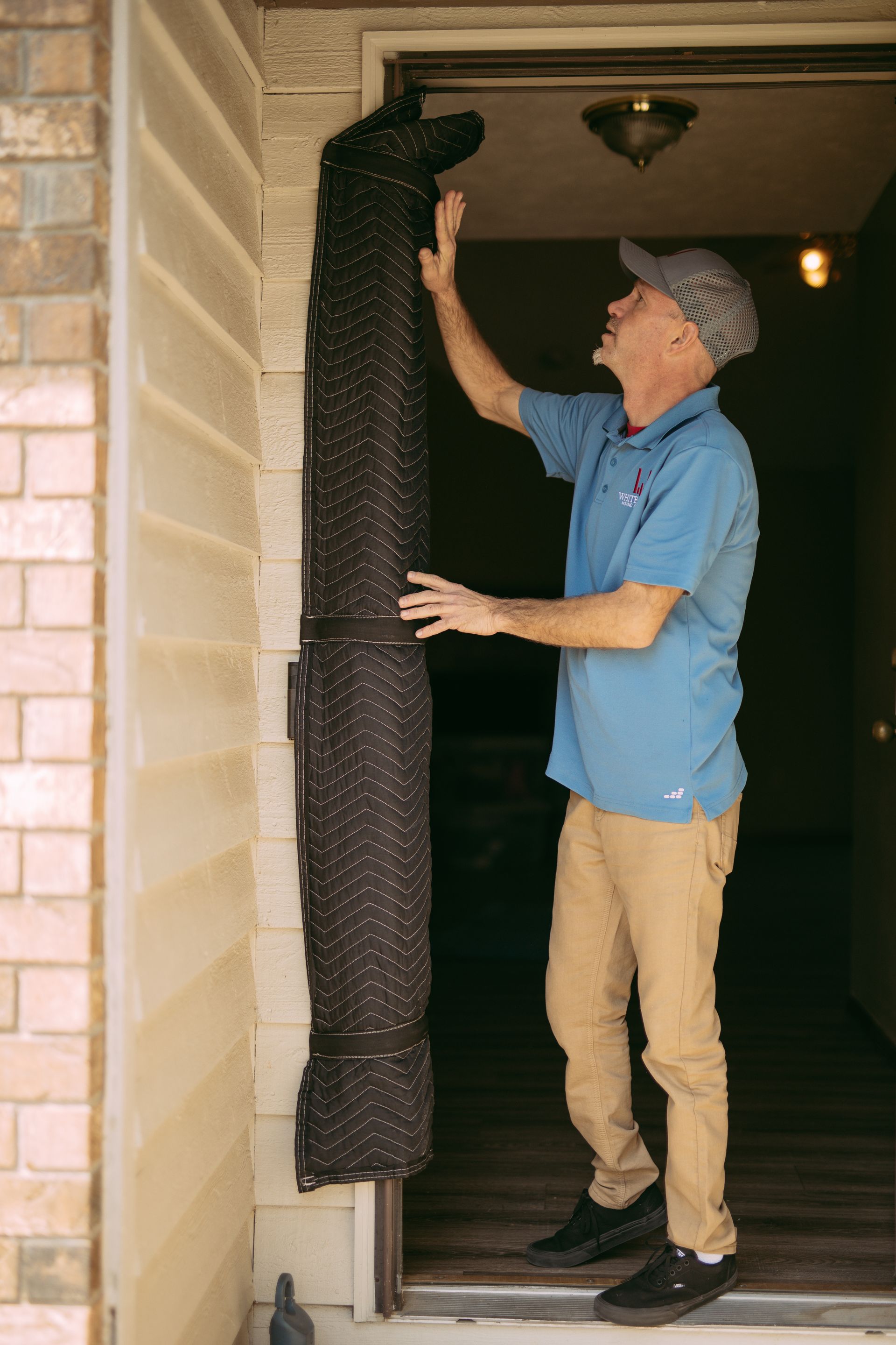 Man hanging a black weatherstrip over a doorway while standing on the threshold