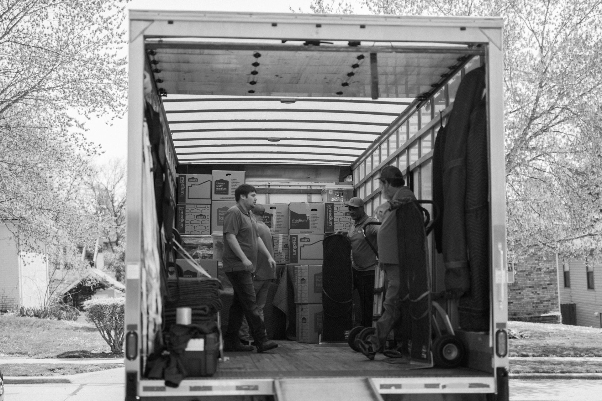 People unloading equipment from the back of a moving truck in a driveway