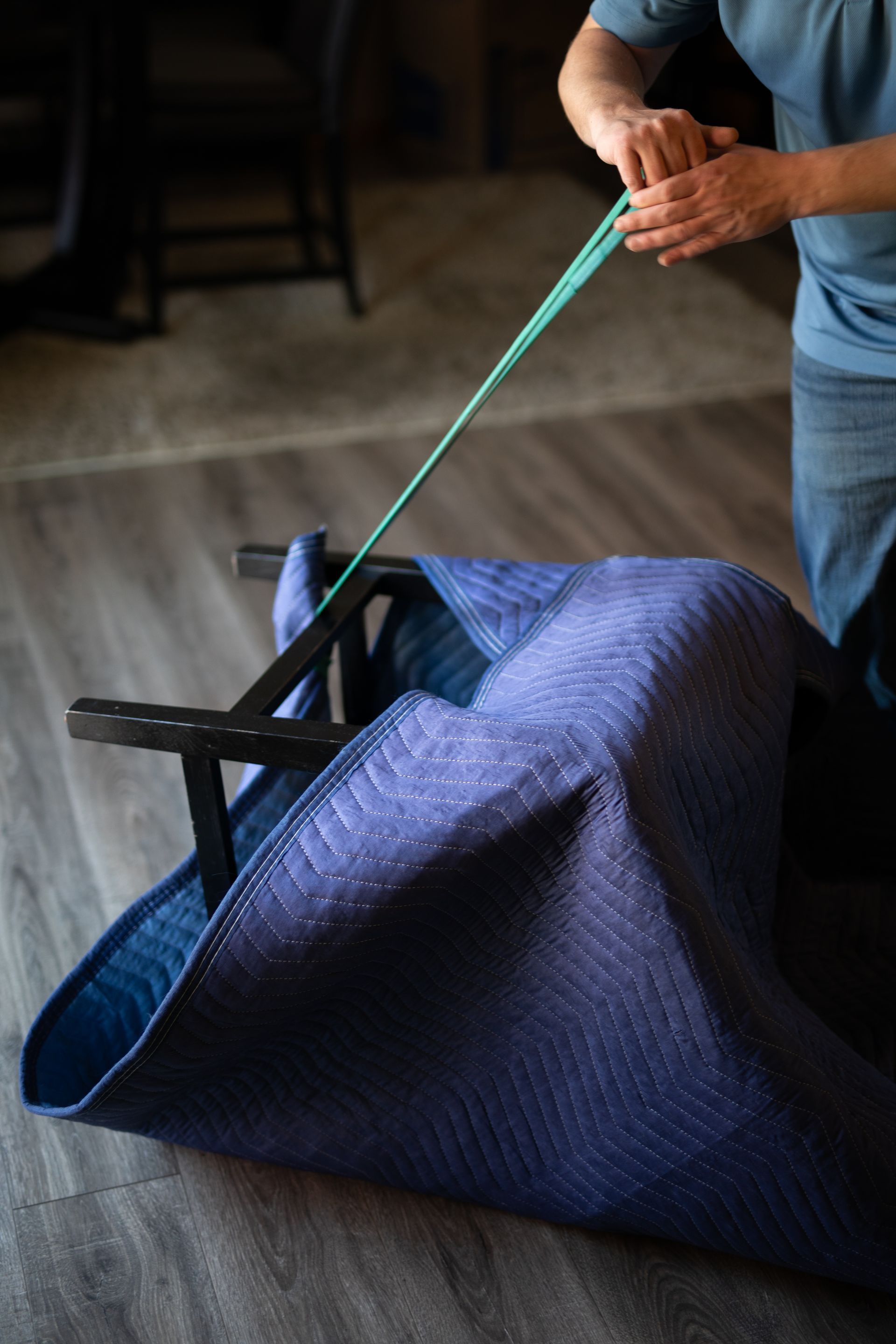 Person tying a blue tarp-covered bundle with a green rope indoors