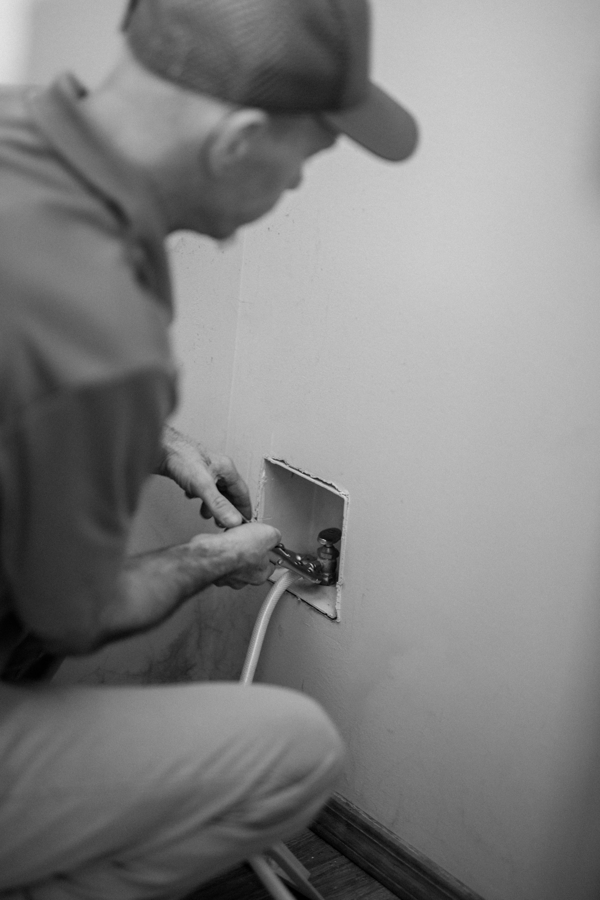 Man kneeling by a wall outlet, working with tools and a cable in a room.