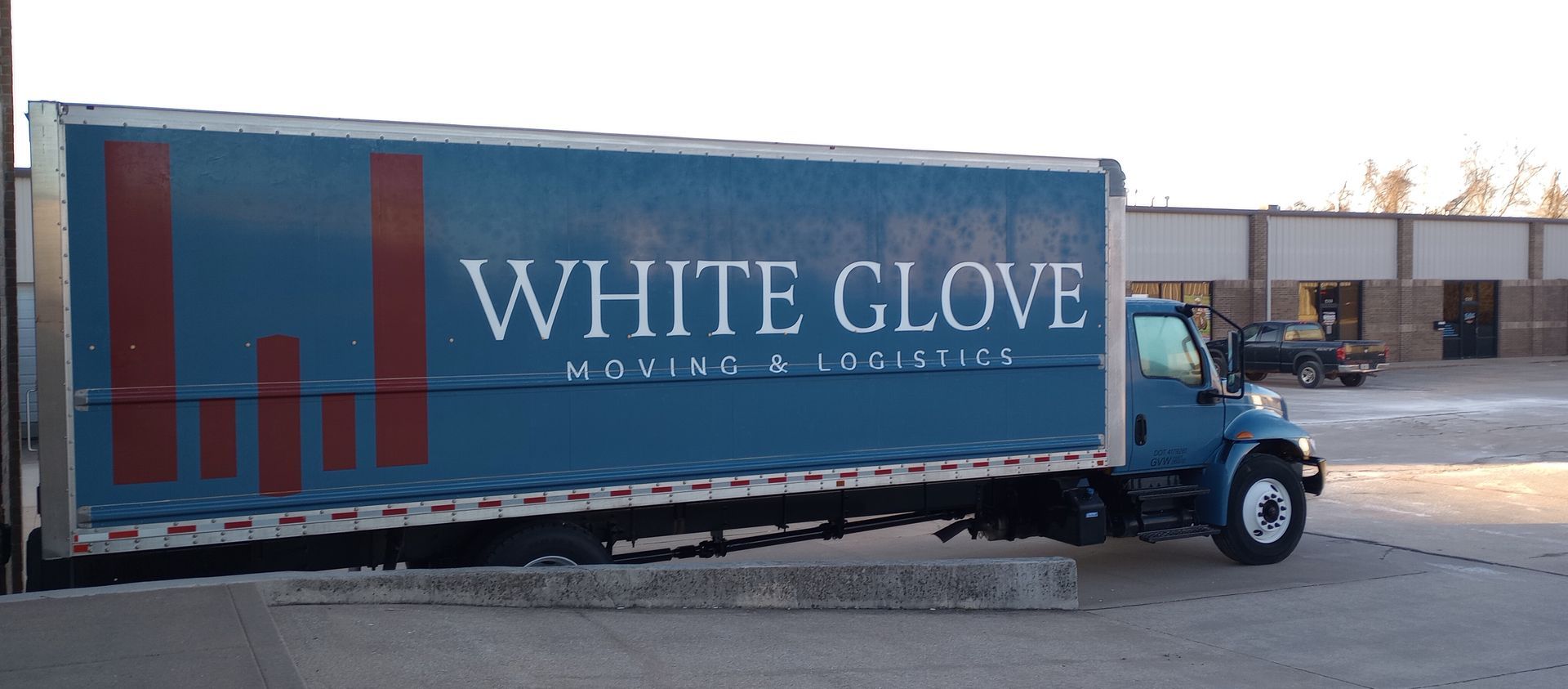 White Glove moving truck parked outdoors, blue cab and trailer with large company logo.
