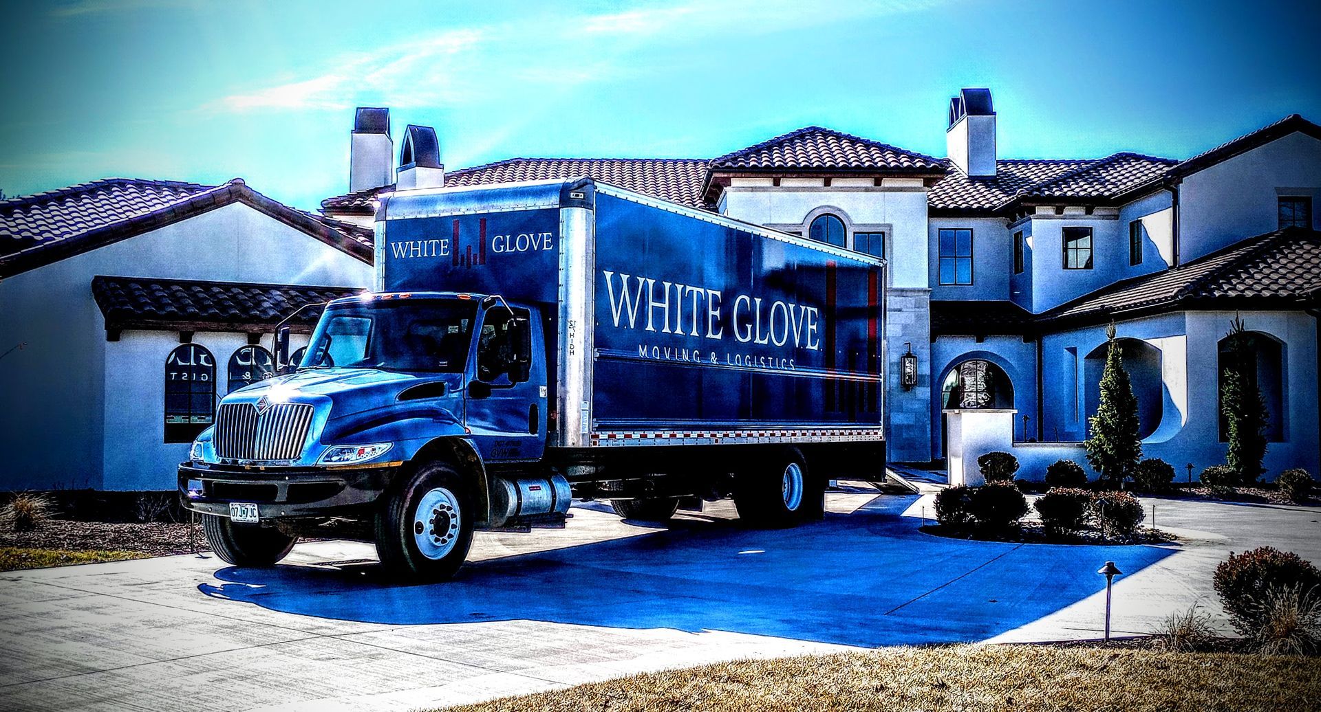 Blue White Claw delivery truck parked in front of a large Mediterranean-style house.