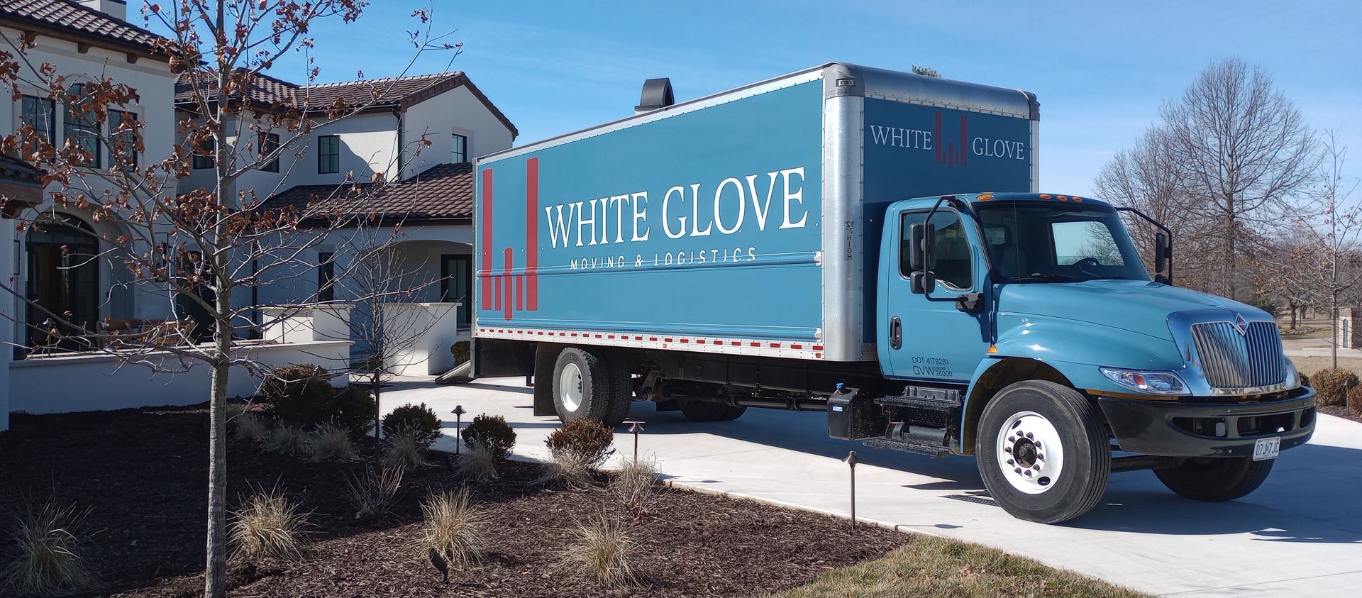 Blue box truck with “GLOVE” branding parked in a suburban driveway beside a house.