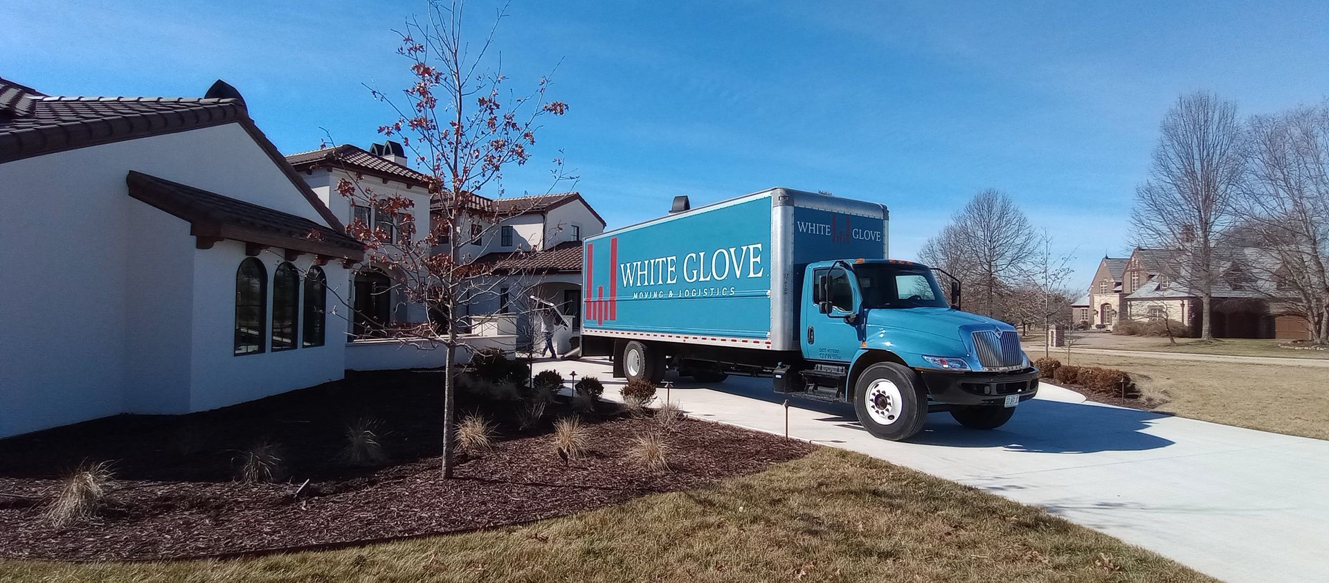 Blue moving truck parked by a white house on a sunny suburban driveway