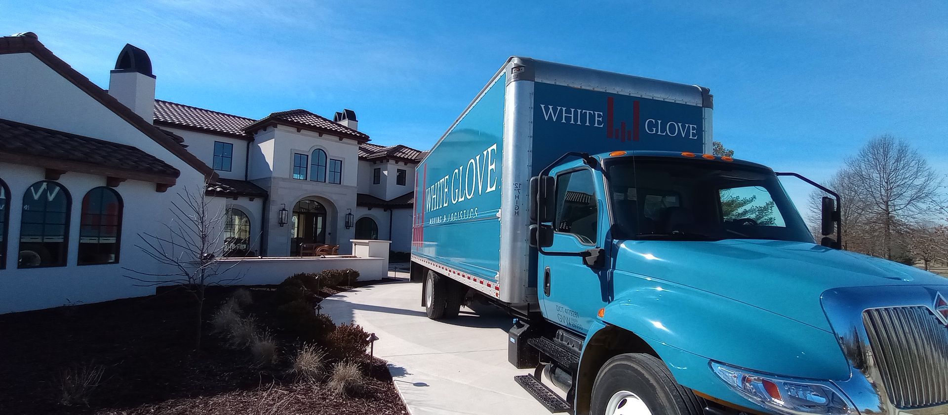 Blue delivery truck parked beside a white stucco building in bright sunlight