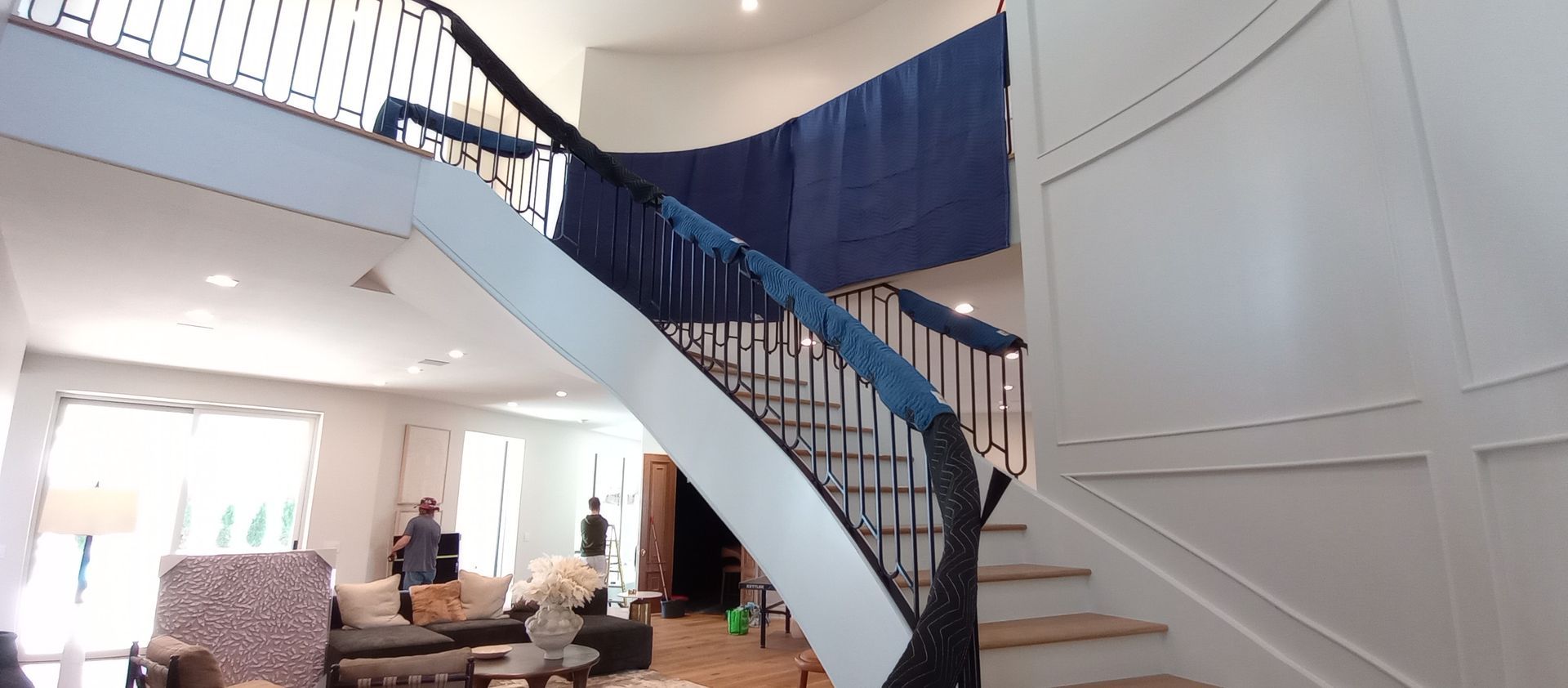 Spacious living room with a curved staircase and a few people gathered near the far wall.