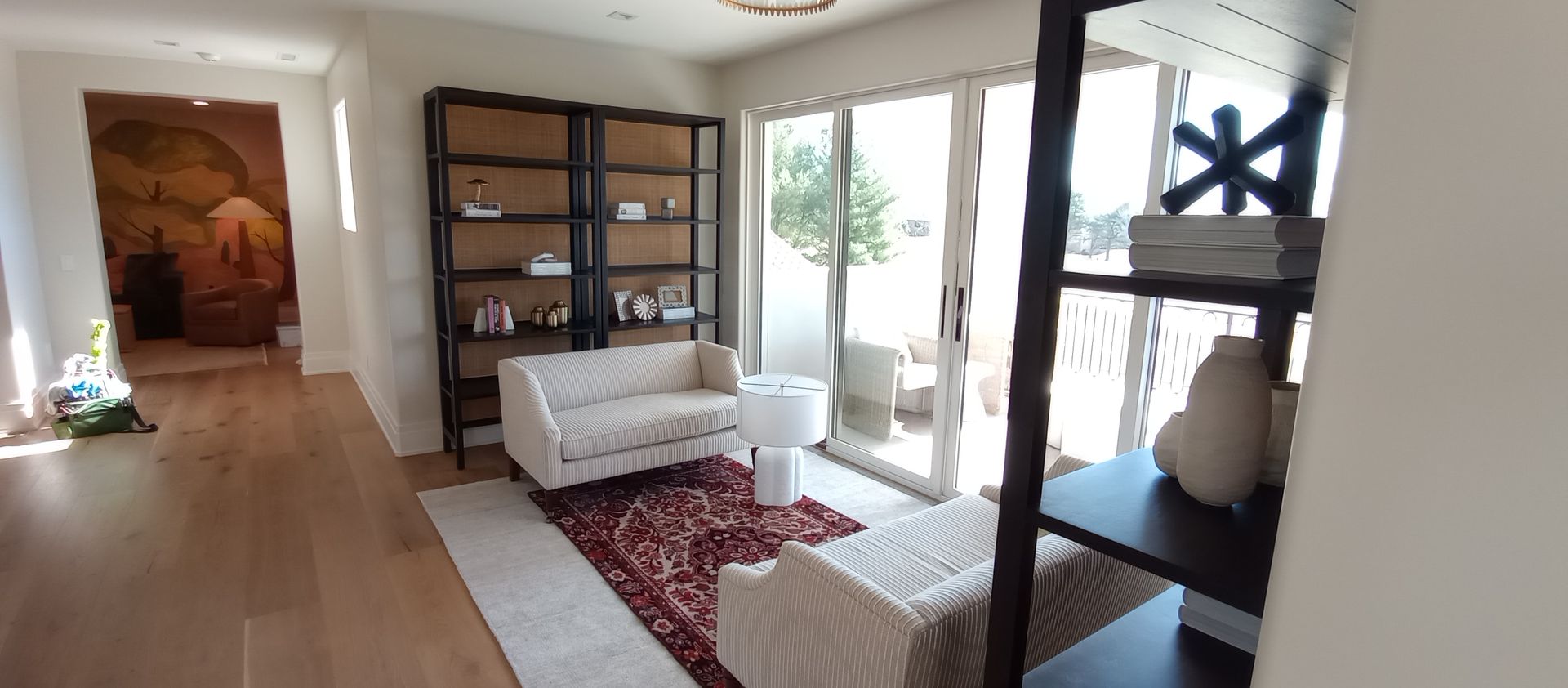 Bright living room with white furniture, red rug, bookshelf, and large windowed door to patio.