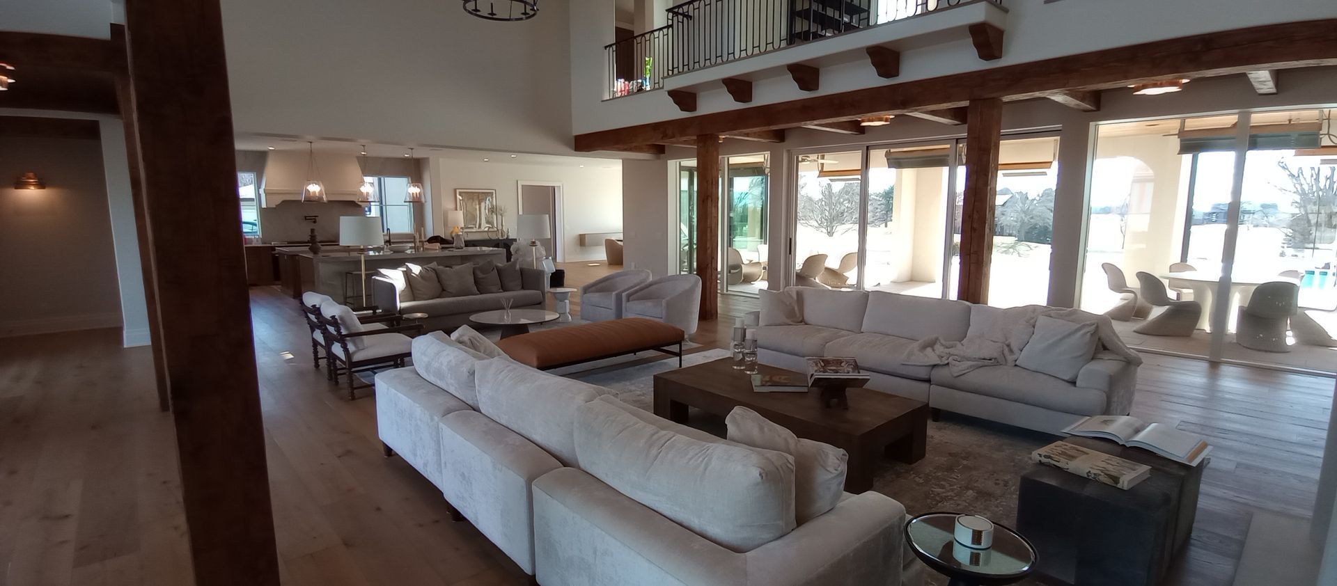 Bright open-plan living room with white sofas, wooden floors, and large windows overlooking water.