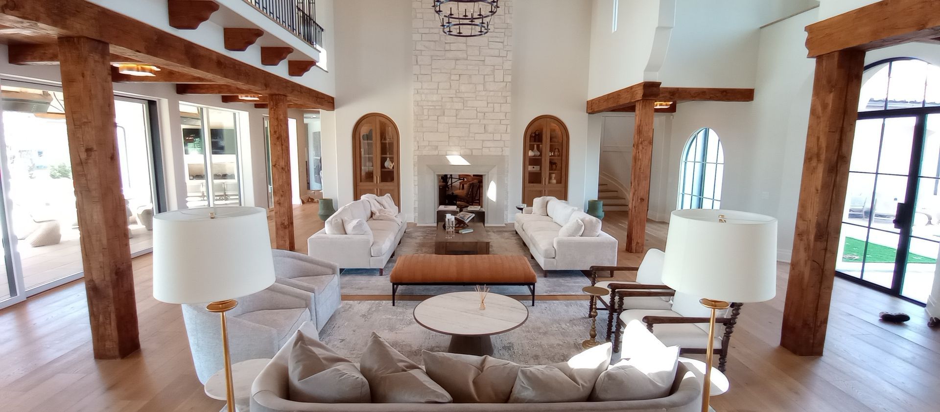 Bright living room with white sofas, wood beams, stone fireplace, and large windows