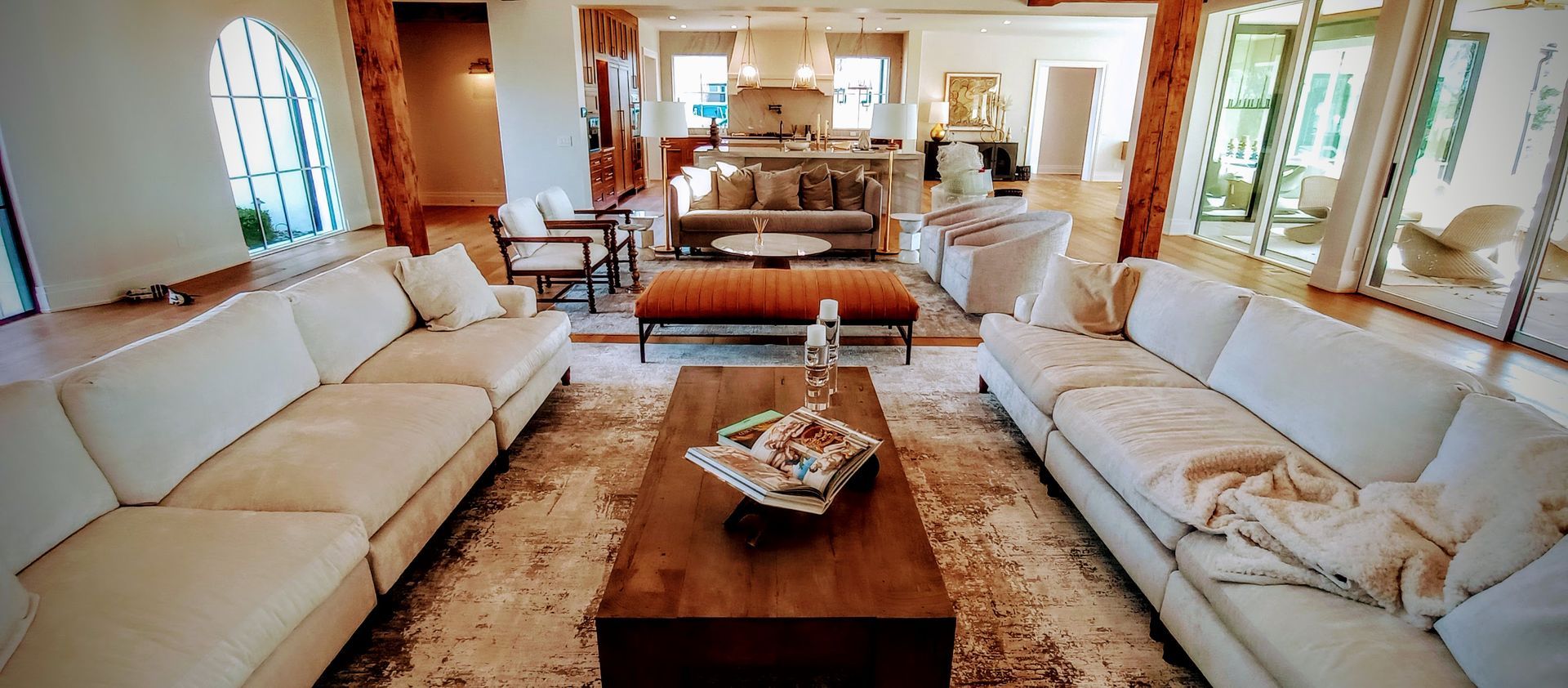 Bright living room with white sofas, wooden coffee table, patterned rug, and large windows