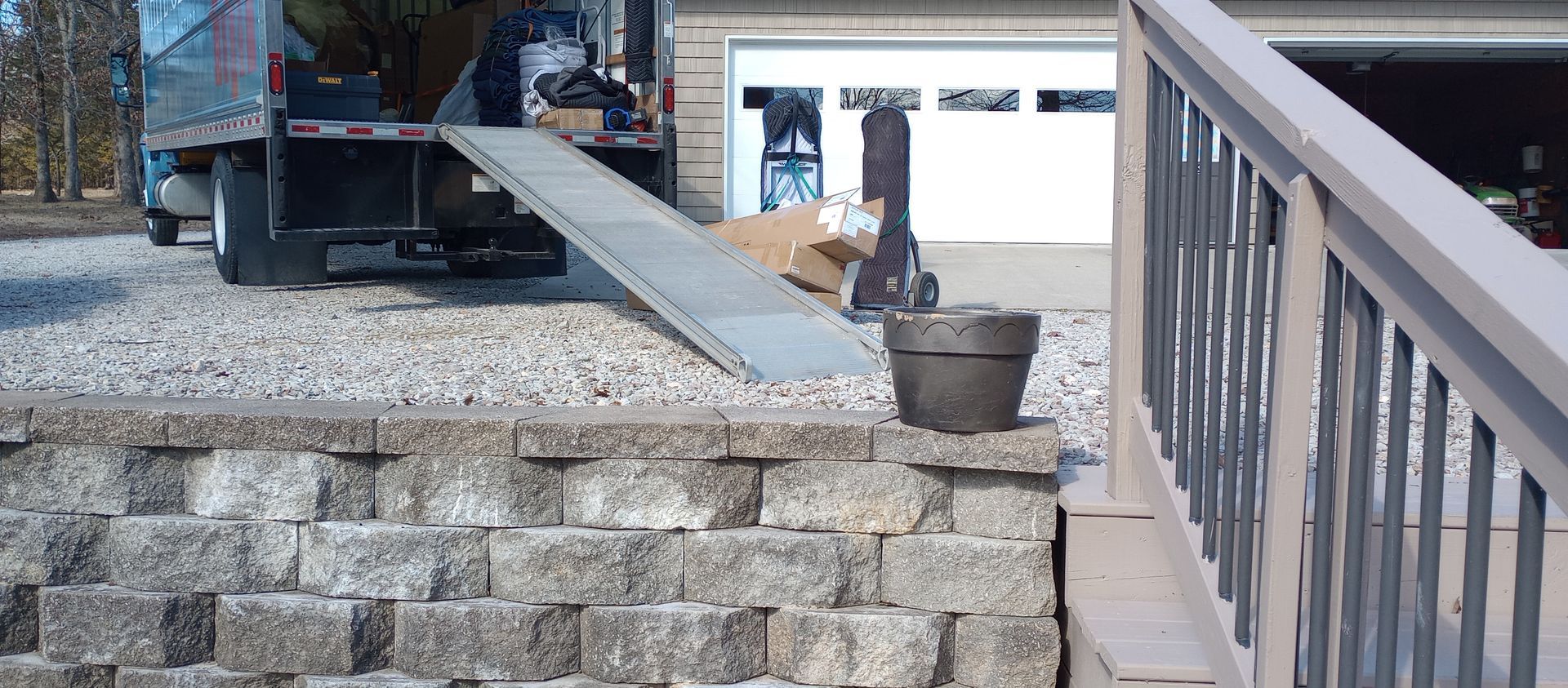 Construction ramp from a truck to a raised stone patio beside a railing and garage