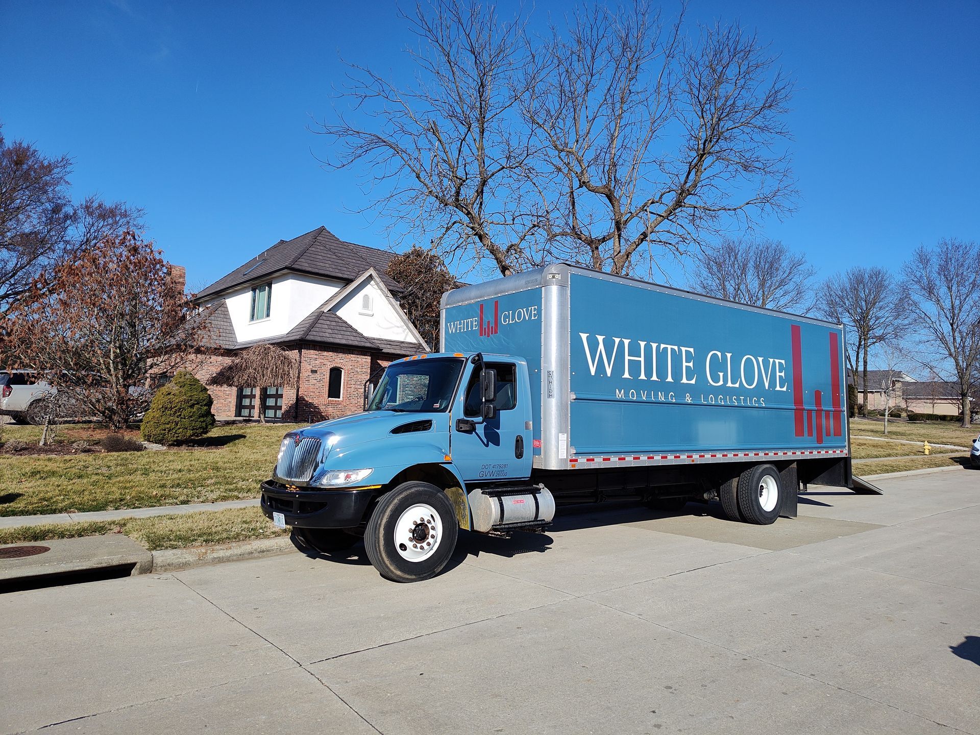 Blue White Cloud moving truck parked on a suburban street beside houses and trees