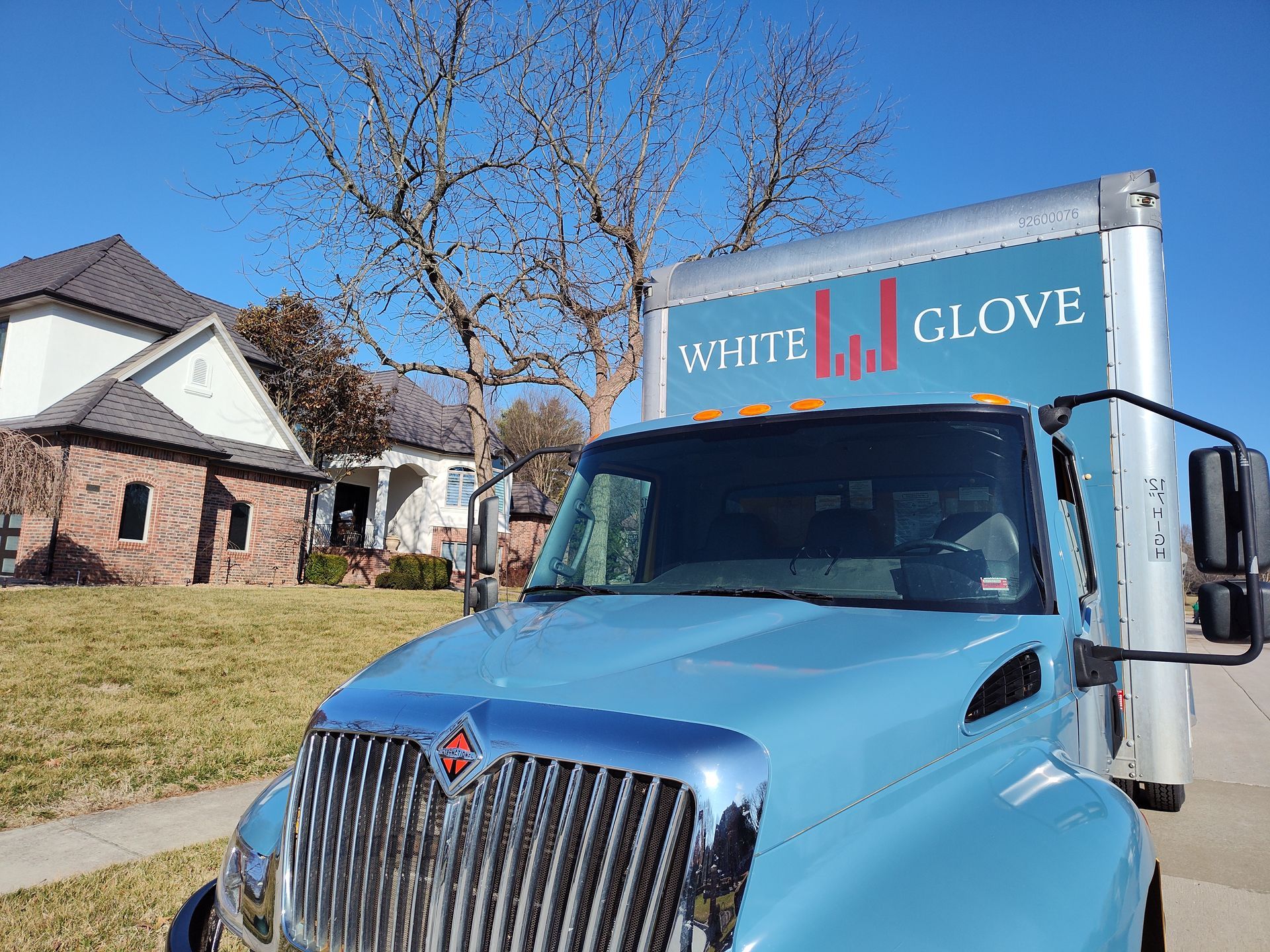 Blue moving truck parked in front of a house on a sunny residential street