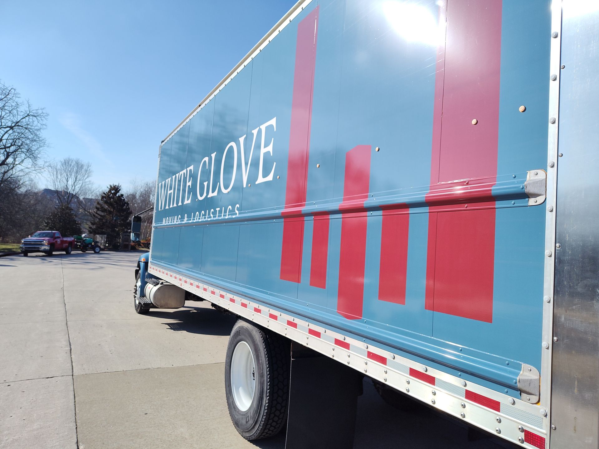 Blue REI CO-OP truck parked in a lot, shown from the side with large red lettering and sunny sky.