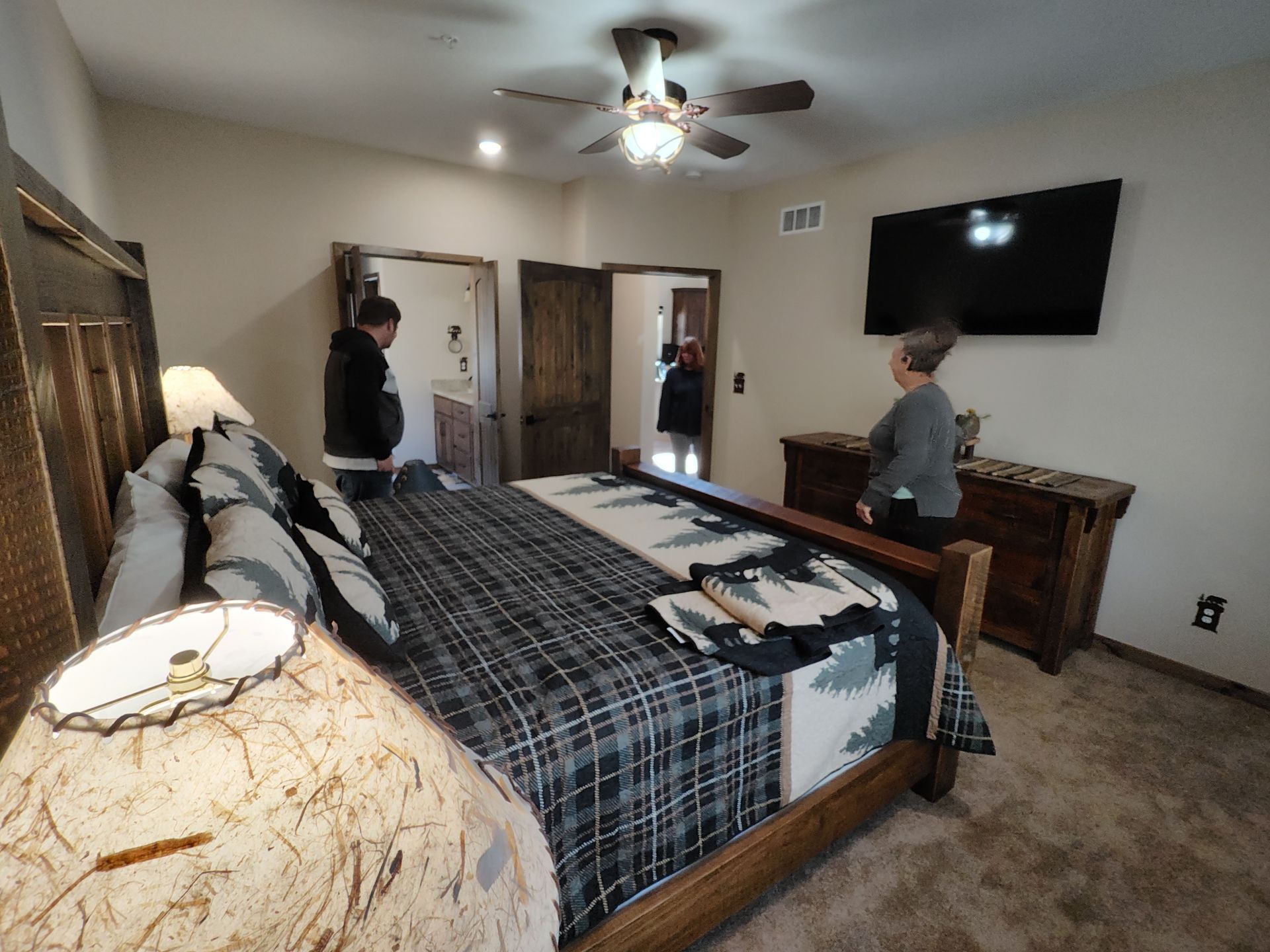 Bedroom with a large bed, TV on the wall, and two people standing near the doorway.