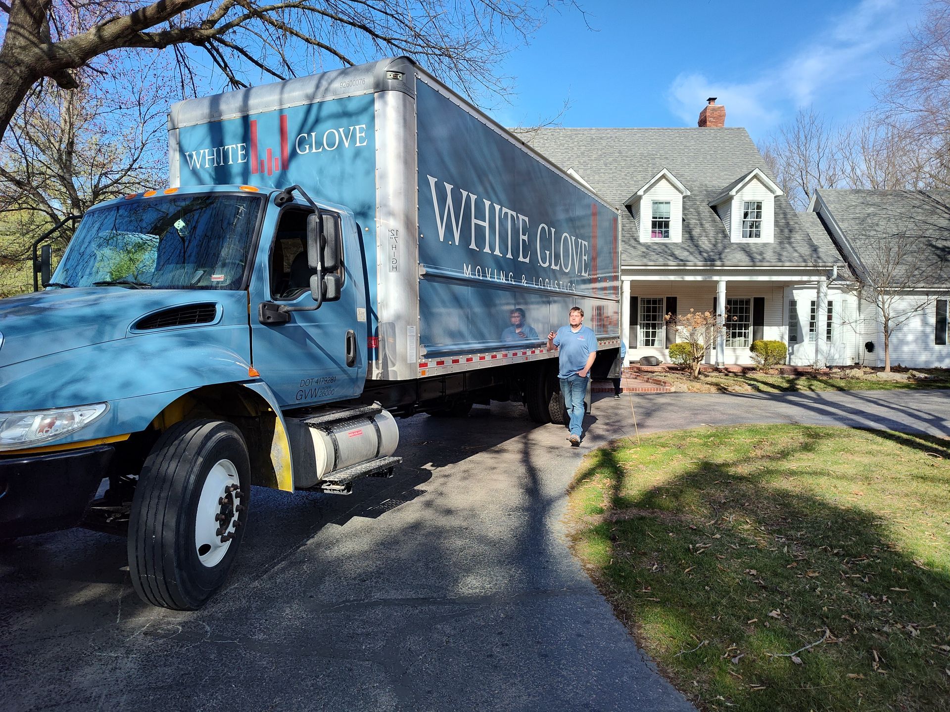 Blue moving truck parked in driveway beside a gray house on a sunny day