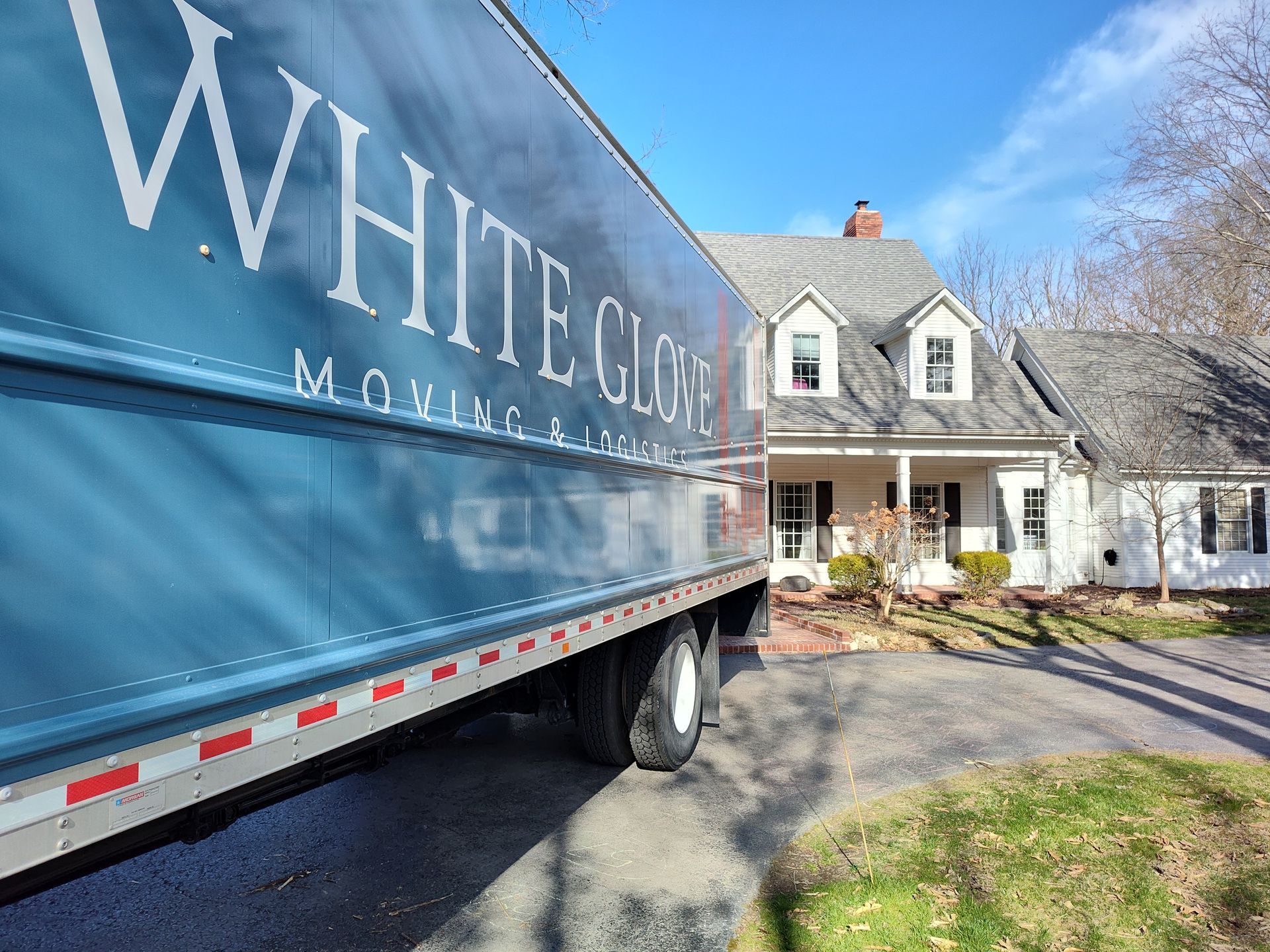 White moving truck parked in driveway beside a house on a sunny day
