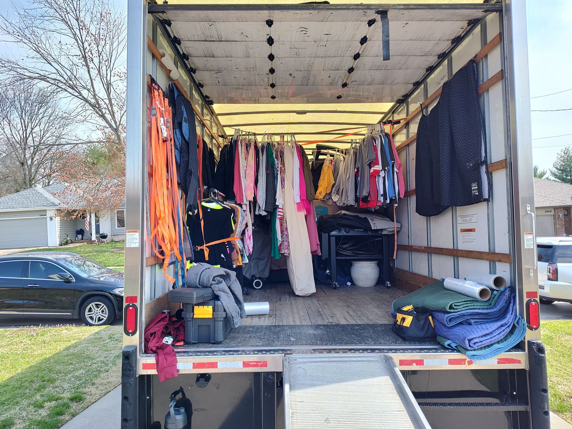 Open box truck interior with hanging clothes, folded blankets, and storage bins inside.
