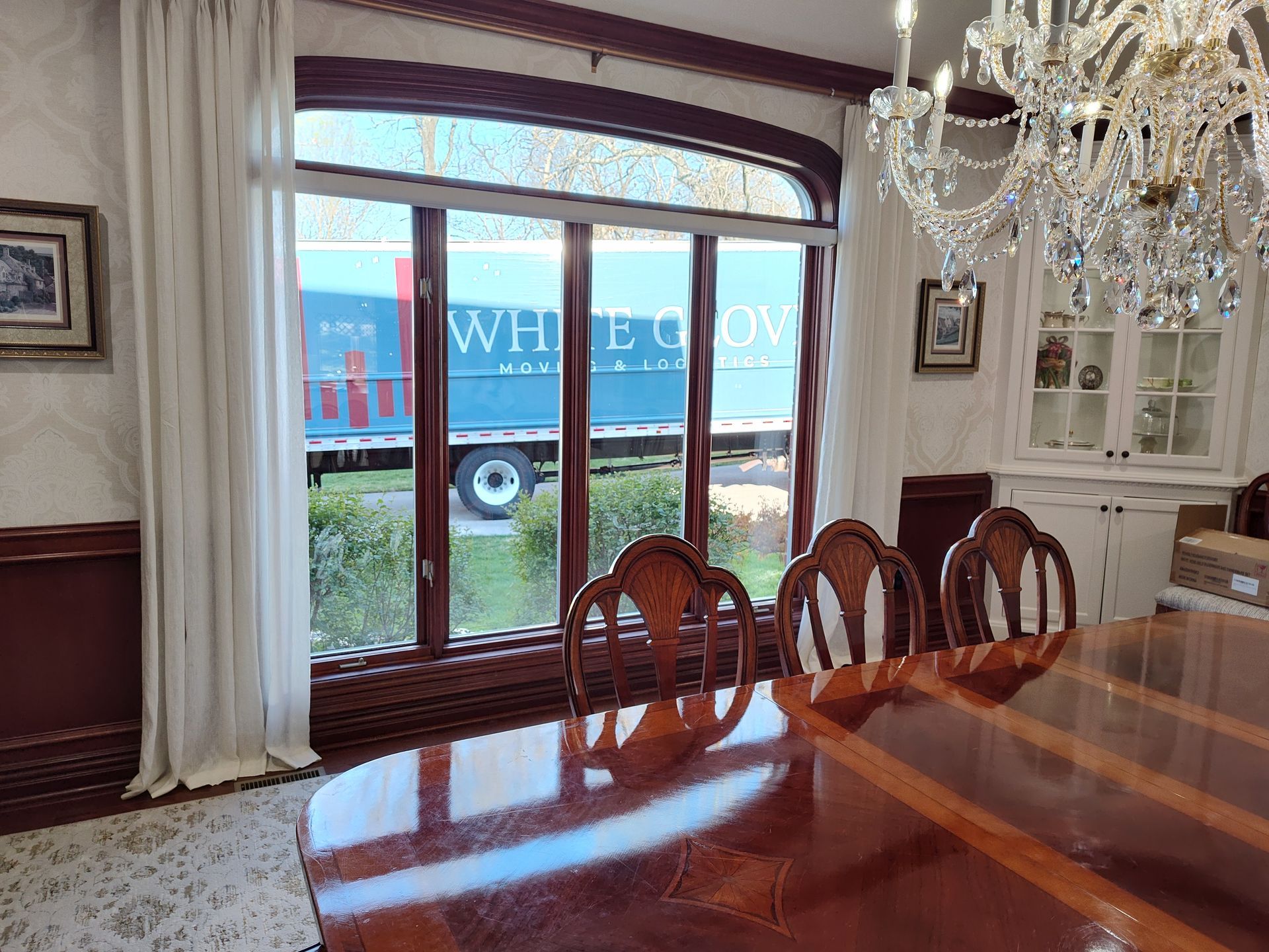 Elegant dining room with chandelier, polished wood table, and large window overlooking a truck outside